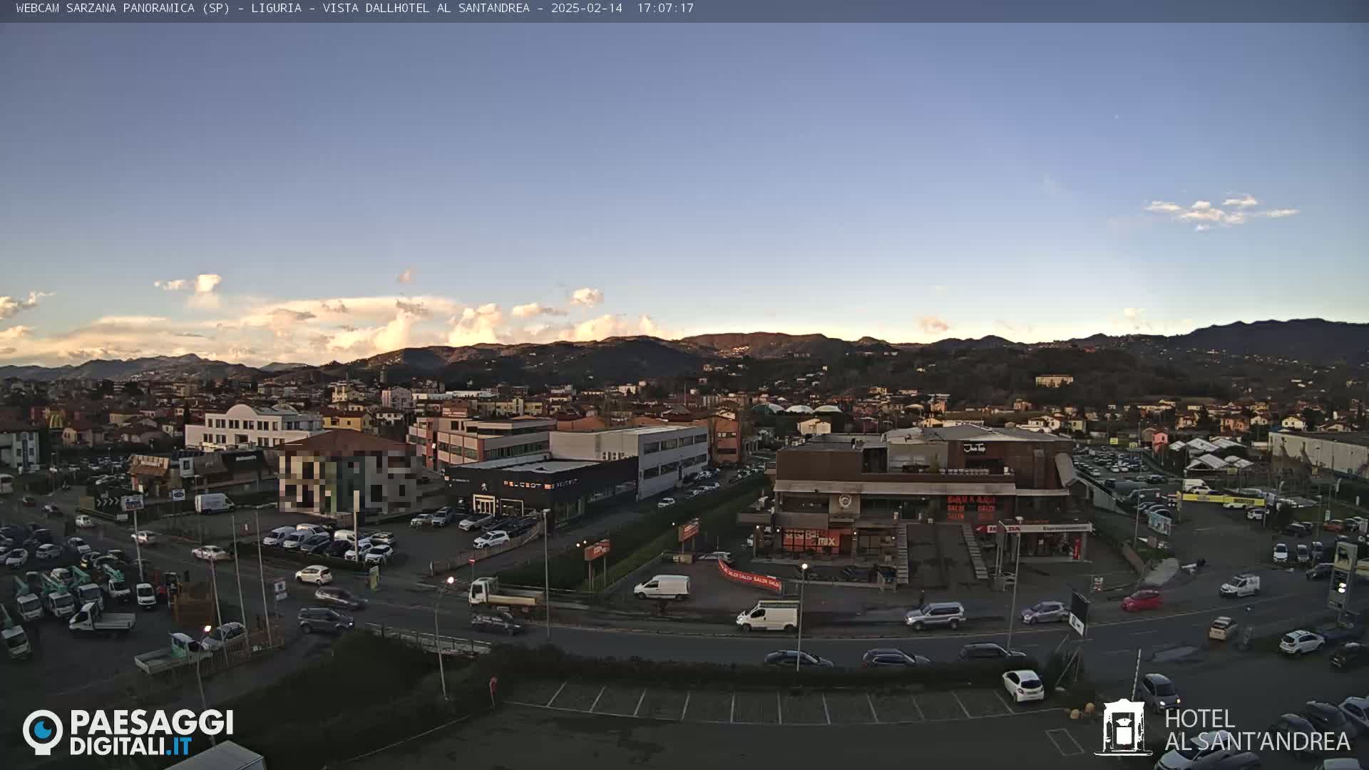 A panoramic view of a town nestled in a valley, under a mostly clear sky with a few scattered clouds at sunset.