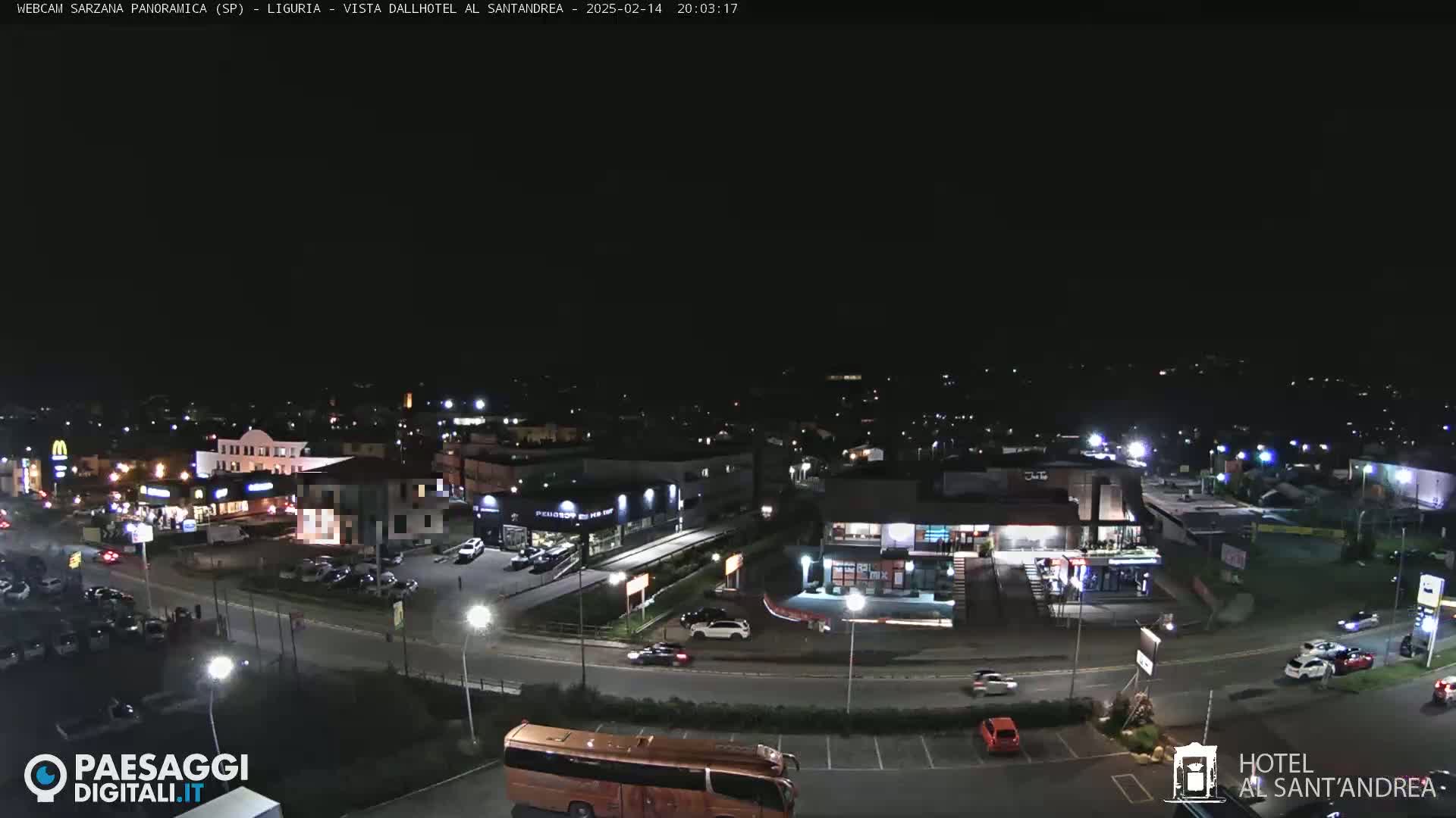 A nighttime aerial view of a town's illuminated streets and businesses, featuring vehicles and a large bus.