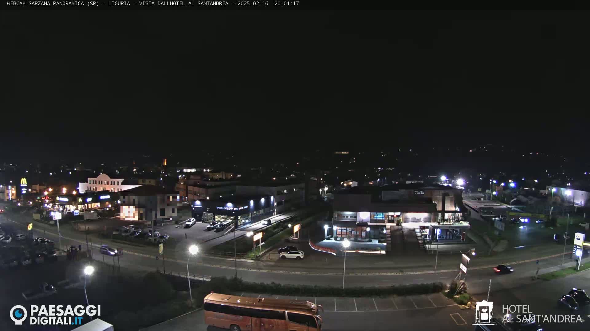 A nighttime aerial view of a town’s street scene with cars, buildings, and a large bus.