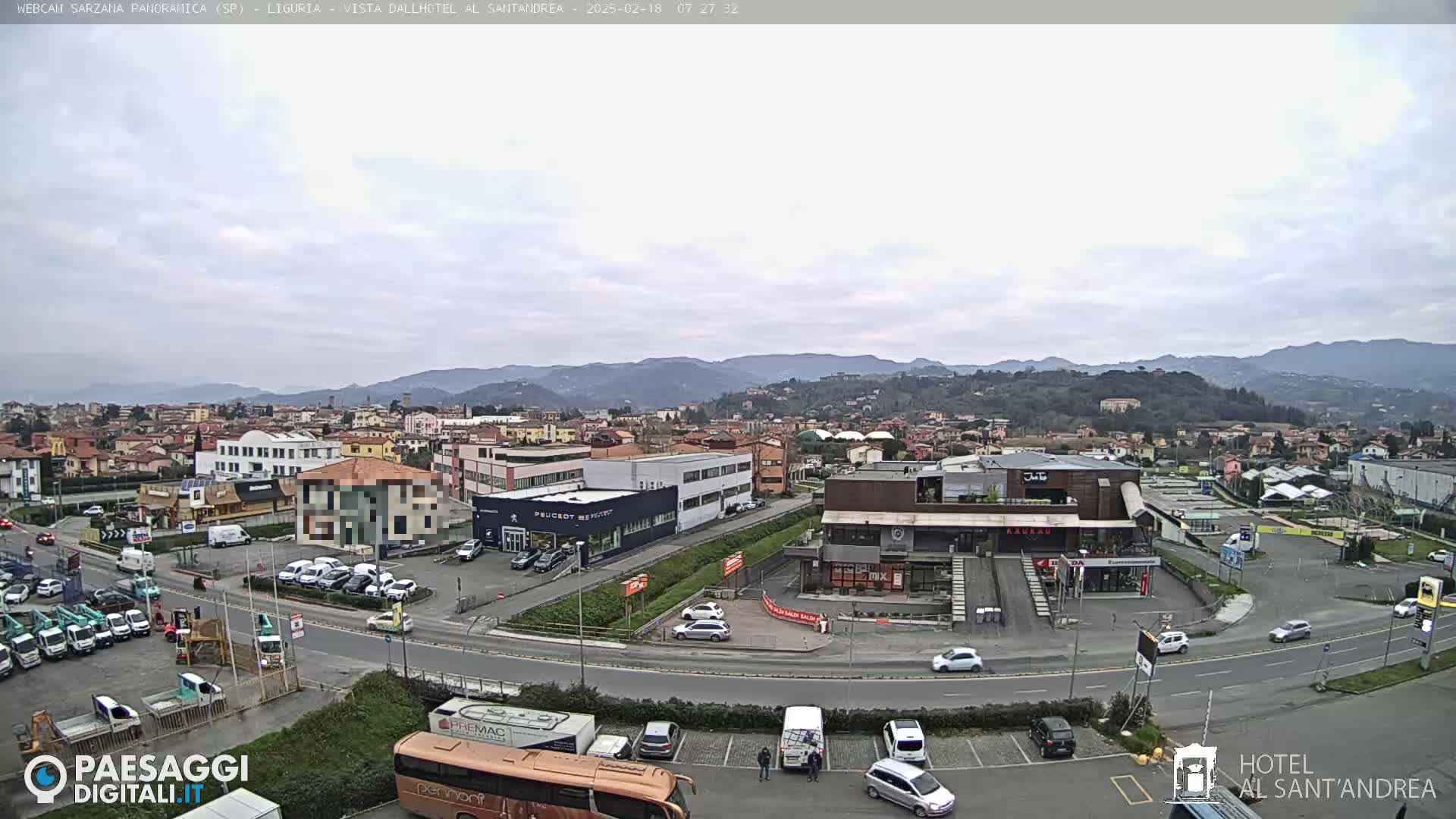 A wide, overcast view of a town with numerous buildings, parking lots, and roads, backed by distant hills.
