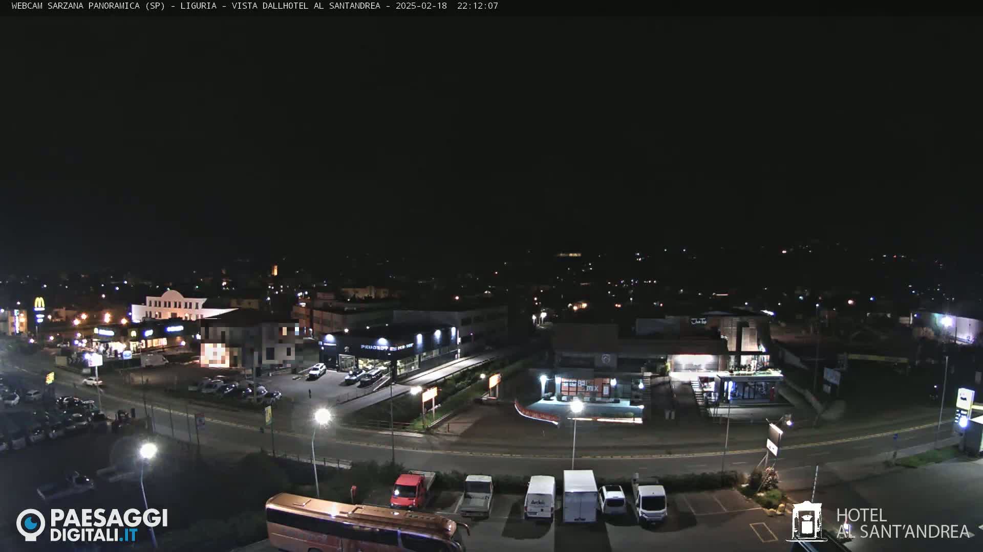A nighttime, overhead view of a town's outskirts, featuring illuminated buildings, roads, and parked vehicles.