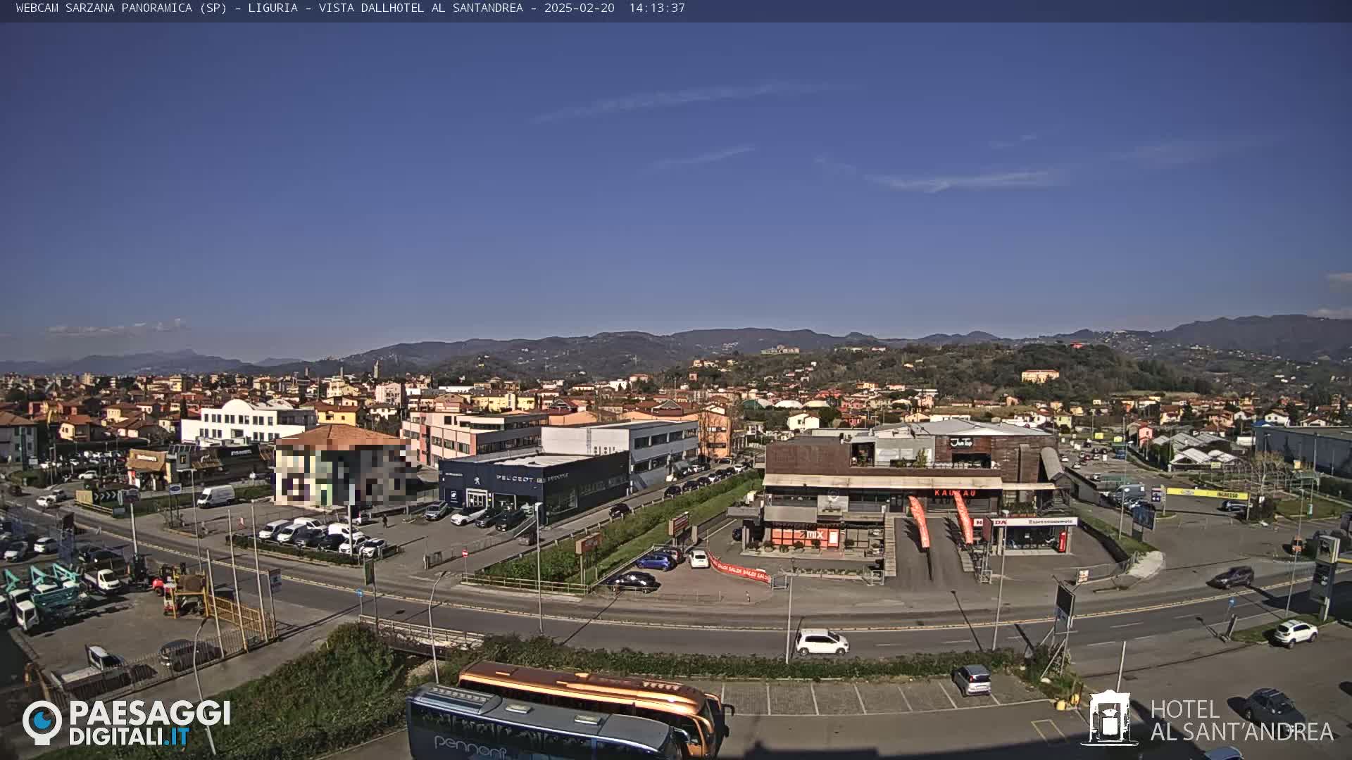 A sunny view of a town nestled in a valley, with mountains in the background and cars parked in a lot in the foreground.