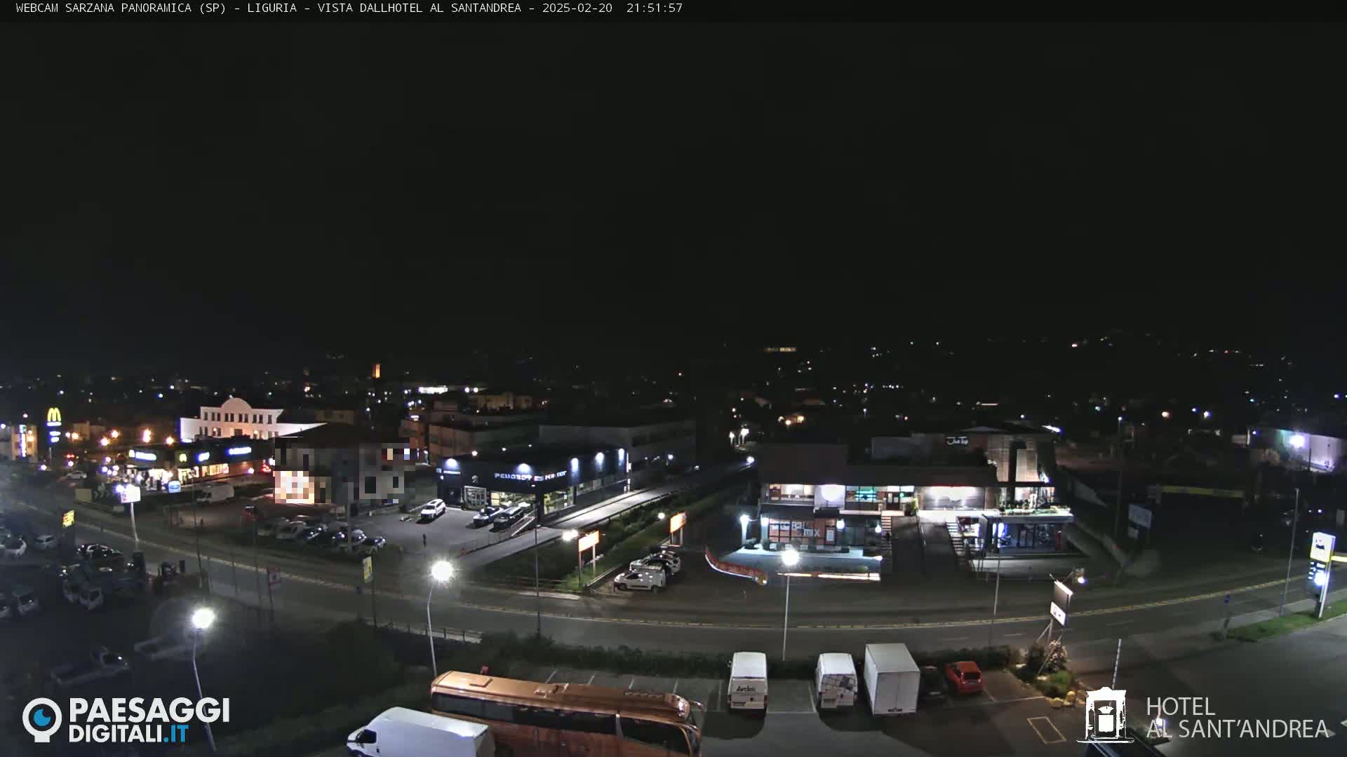 A nighttime aerial view of a town's outskirts showing roads, buildings, and parked vehicles under a clear, dark sky.