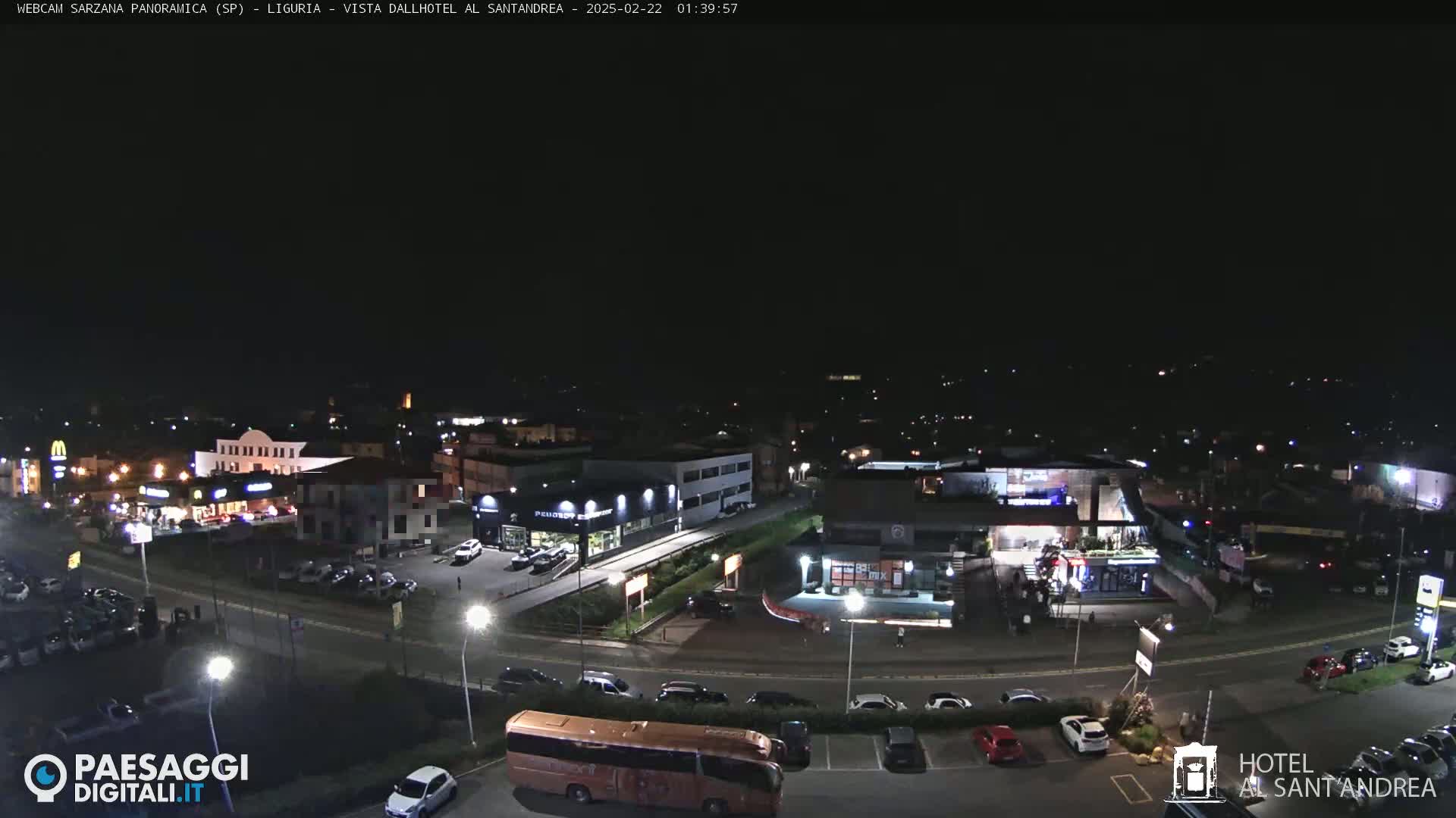 A nighttime aerial view of a town's illuminated streets, parking lots, and buildings, including restaurants and a hotel.