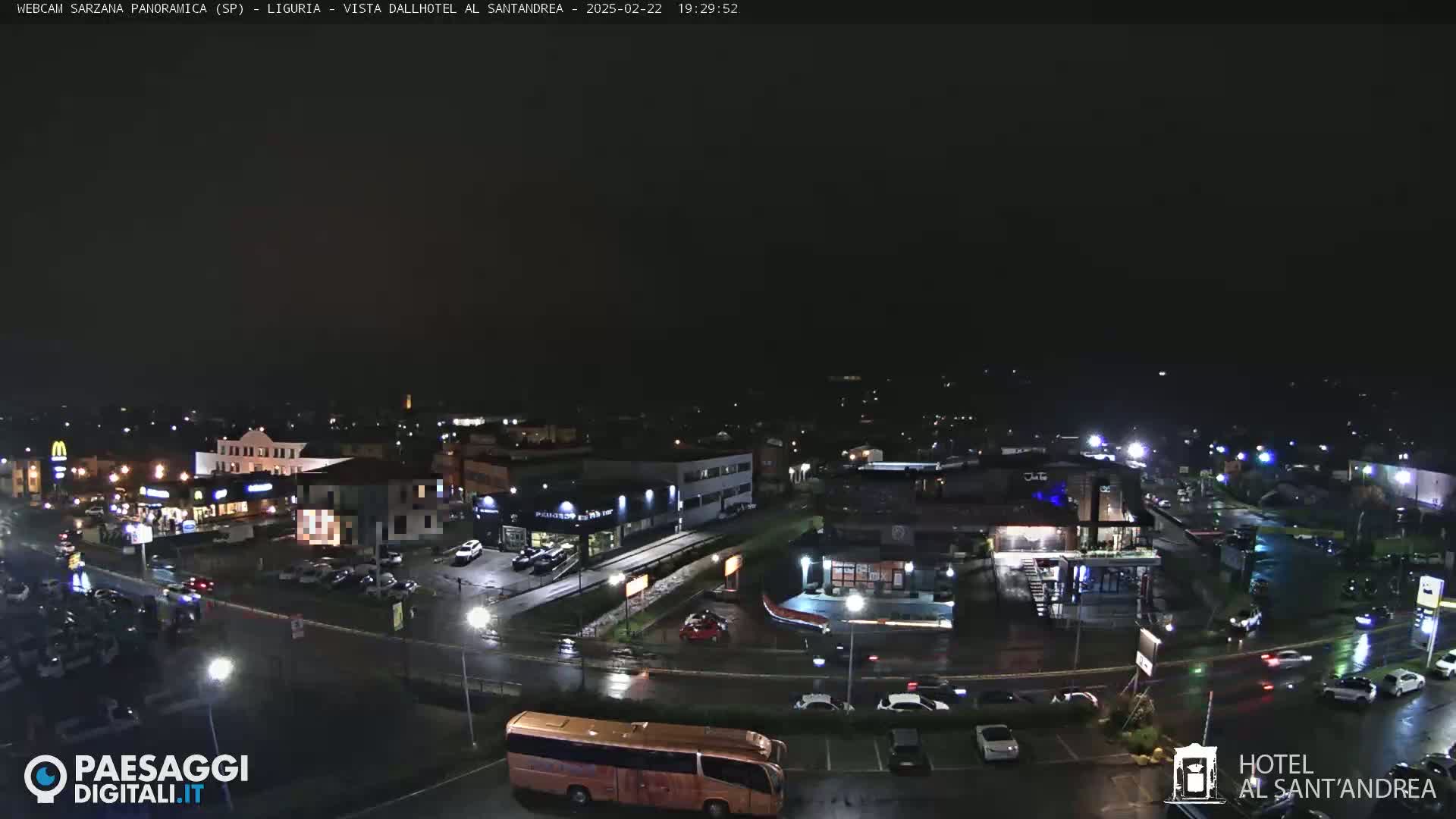 A nighttime, wet view of a town's streets and buildings, with cars and a bus visible.