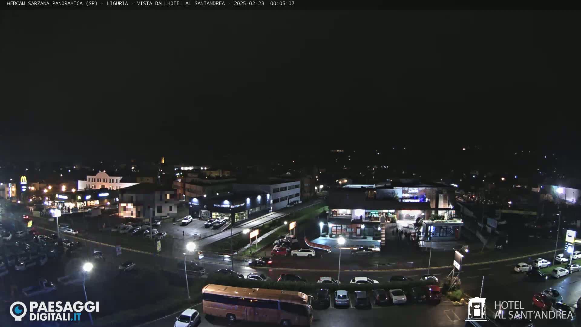 A nighttime, high-angle view of a parking lot and several buildings, including a hotel and fast-food restaurant, with cars parked throughout.