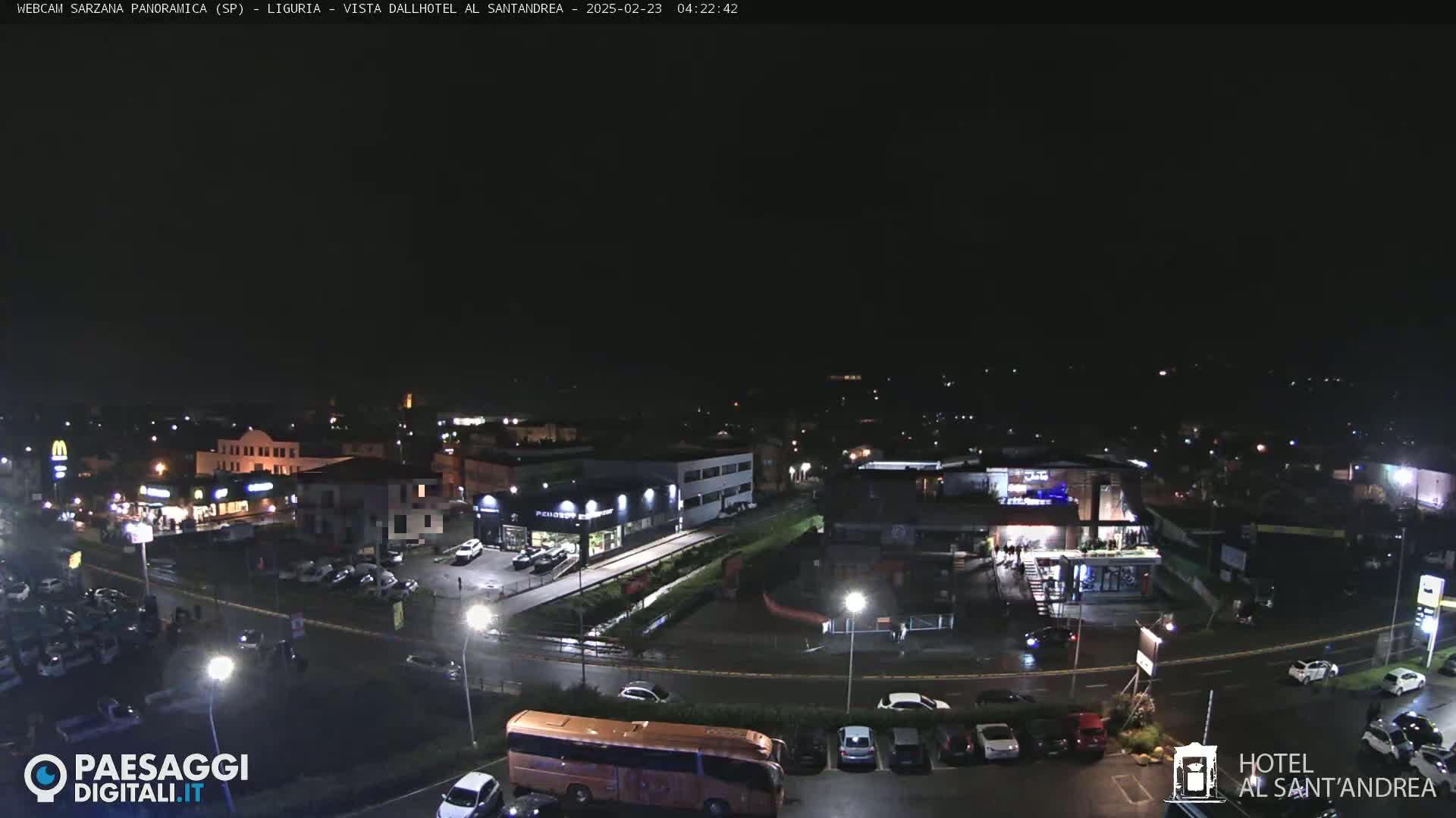 A nighttime, overhead view of a parking lot and roadway, surrounded by buildings and businesses under a clear, dark sky.