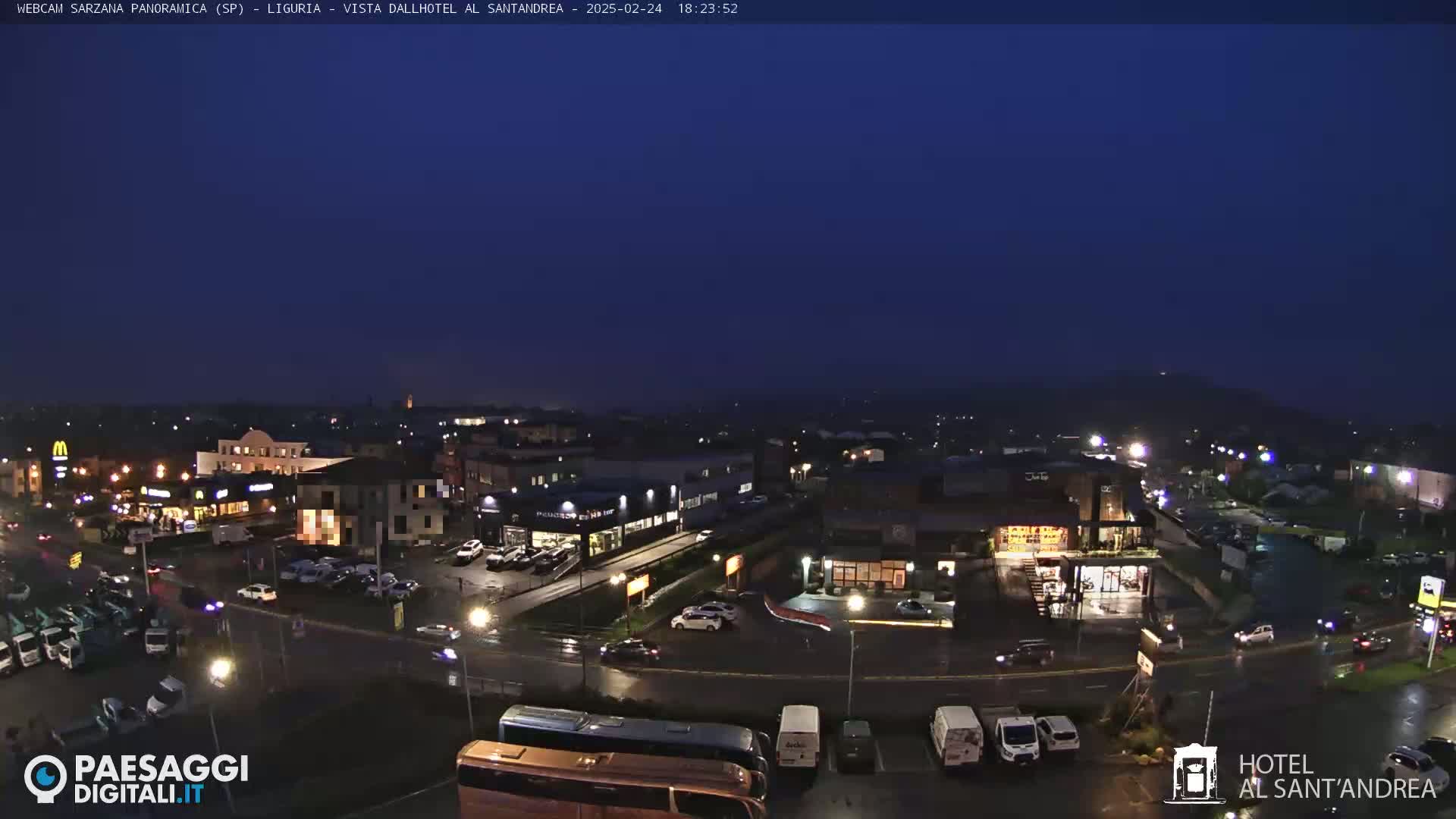 A nighttime, wet view of a town with illuminated buildings, roads, and parked cars.