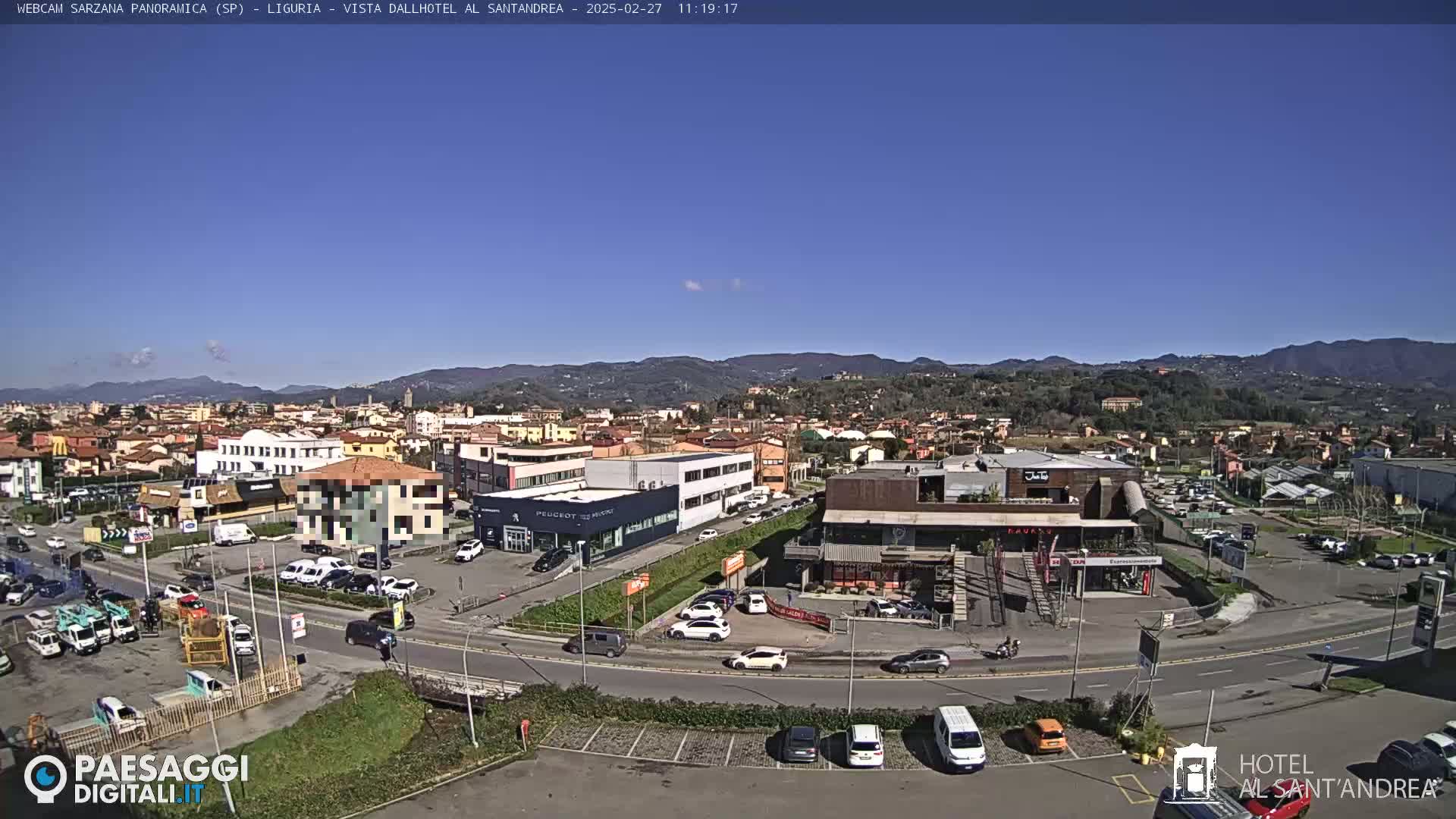 A panoramic view of a town nestled in a valley on a clear, sunny day, with mountains visible in the background.