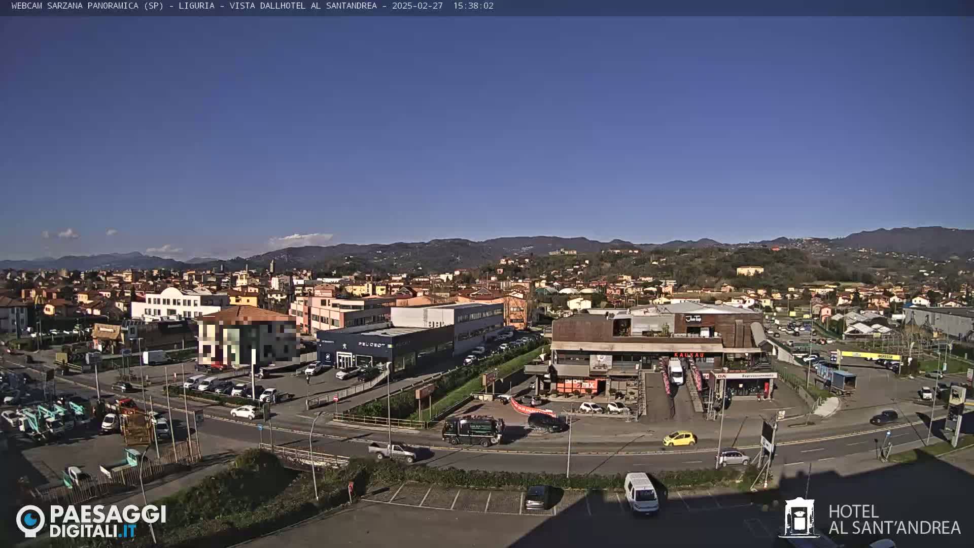 A clear, sunny day reveals a panoramic view of a town nestled in a valley, surrounded by hills and mountains.