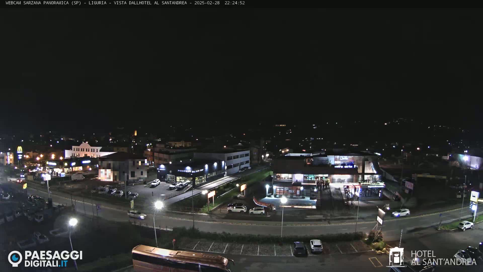 A nighttime, aerial view of a town with illuminated buildings, roads, and parked cars.