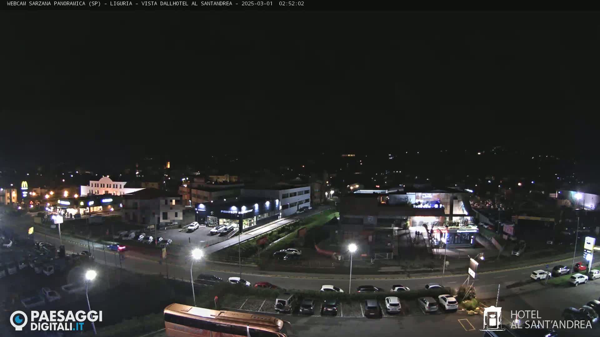 A nighttime aerial view of a town with illuminated buildings and parked cars in a parking lot, under a clear, dark sky.