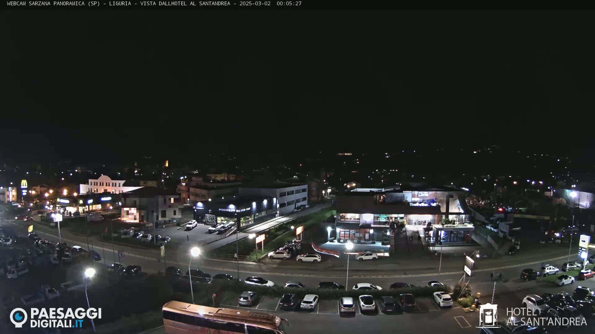A nighttime aerial view of a parking lot and businesses, including restaurants and car dealerships, with a clear sky.
