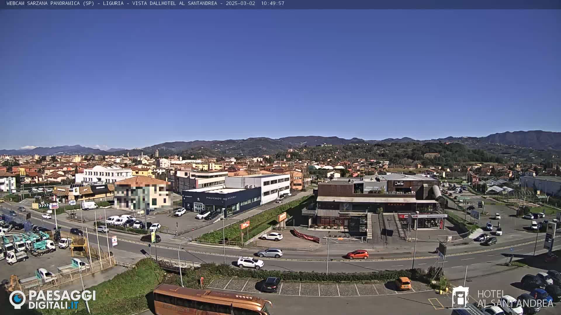 A clear, sunny day reveals a panoramic view of a town nestled amongst rolling hills, with various buildings, roadways, and vehicles visible.