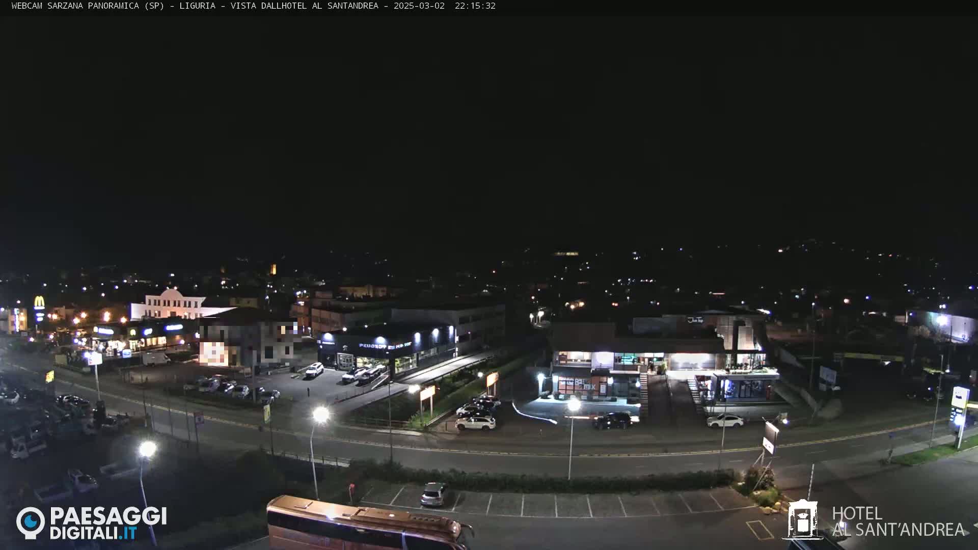 A nighttime, aerial view of a town's street scene showing buildings, cars, and a parking lot with a bus.