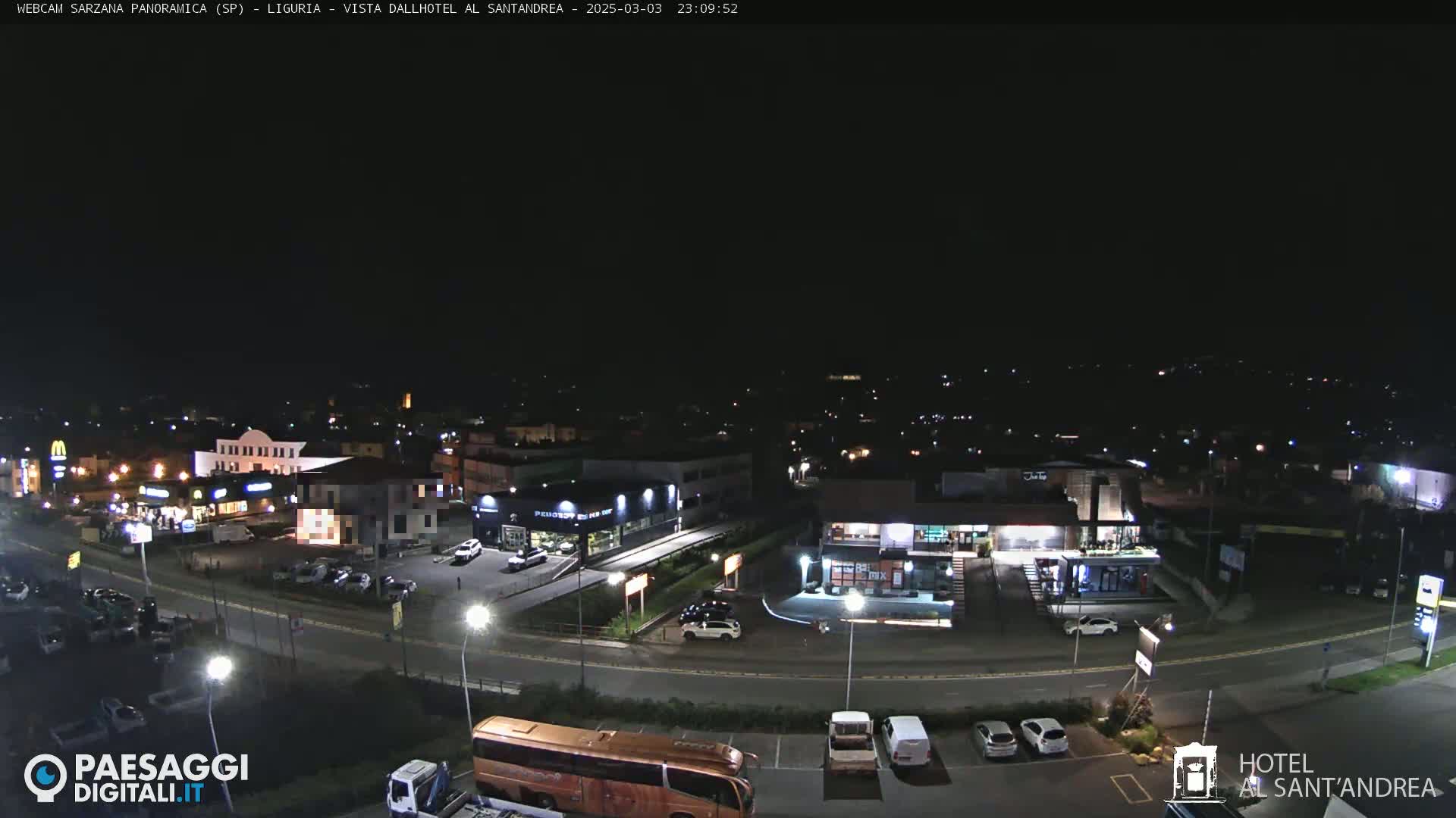 A nighttime, overhead view of a parking lot and surrounding businesses, illuminated by streetlights.