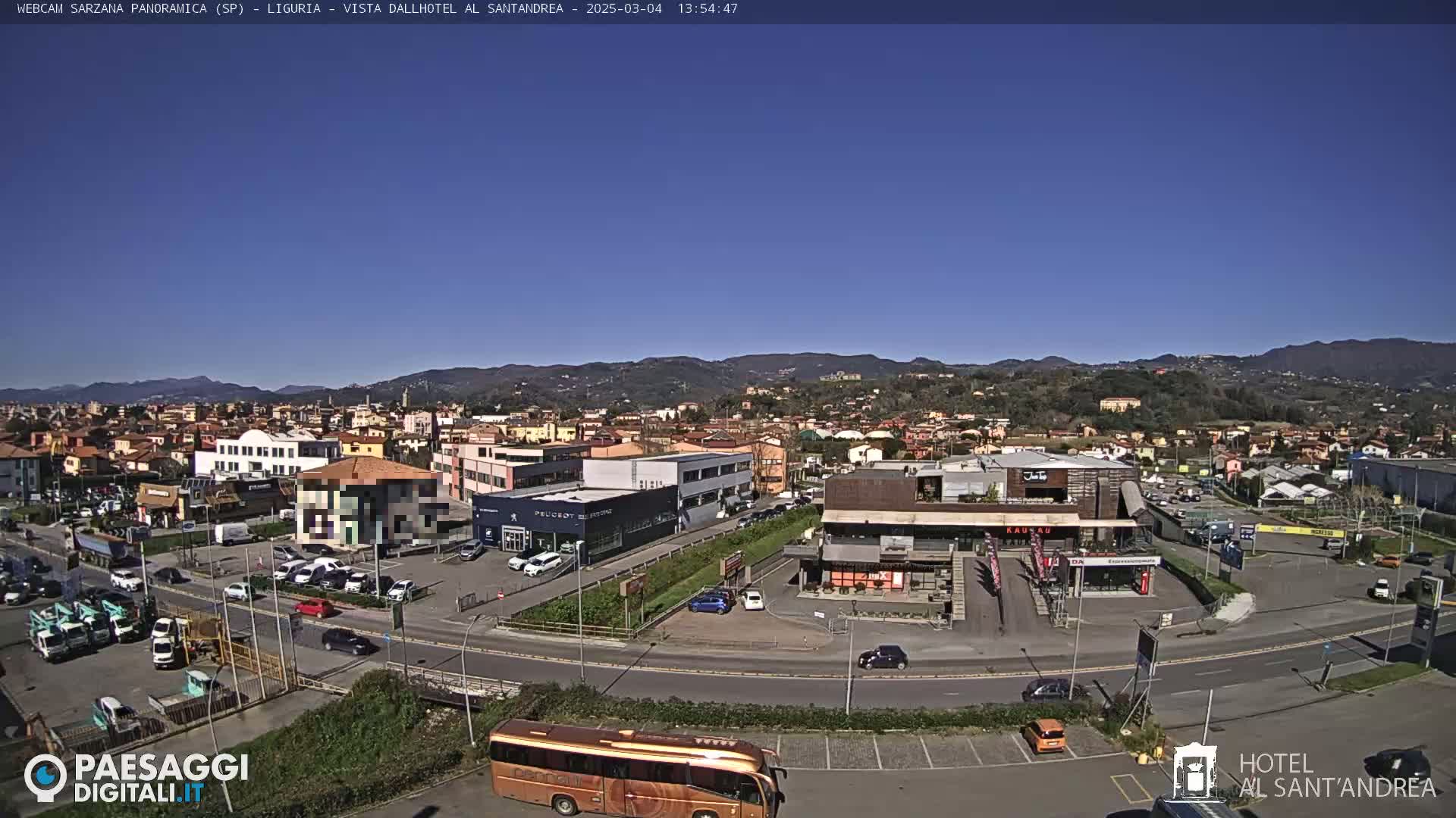 A sunny day reveals a panoramic view of a town with buildings, roads, vehicles, and a bus, nestled among hills.