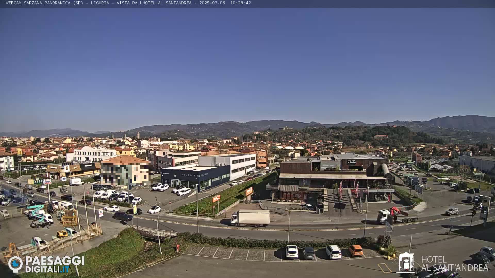 A clear, sunny day reveals a panoramic view of a town nestled in a valley, with mountains in the distance and cars parked in a lot.