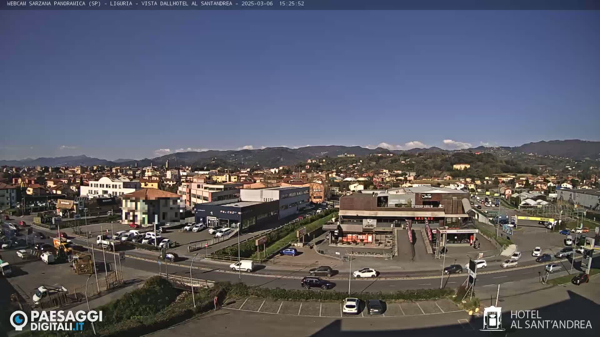 A sunny, clear day overlooking a town with buildings, cars in parking lots and on roads, and mountains in the background.
