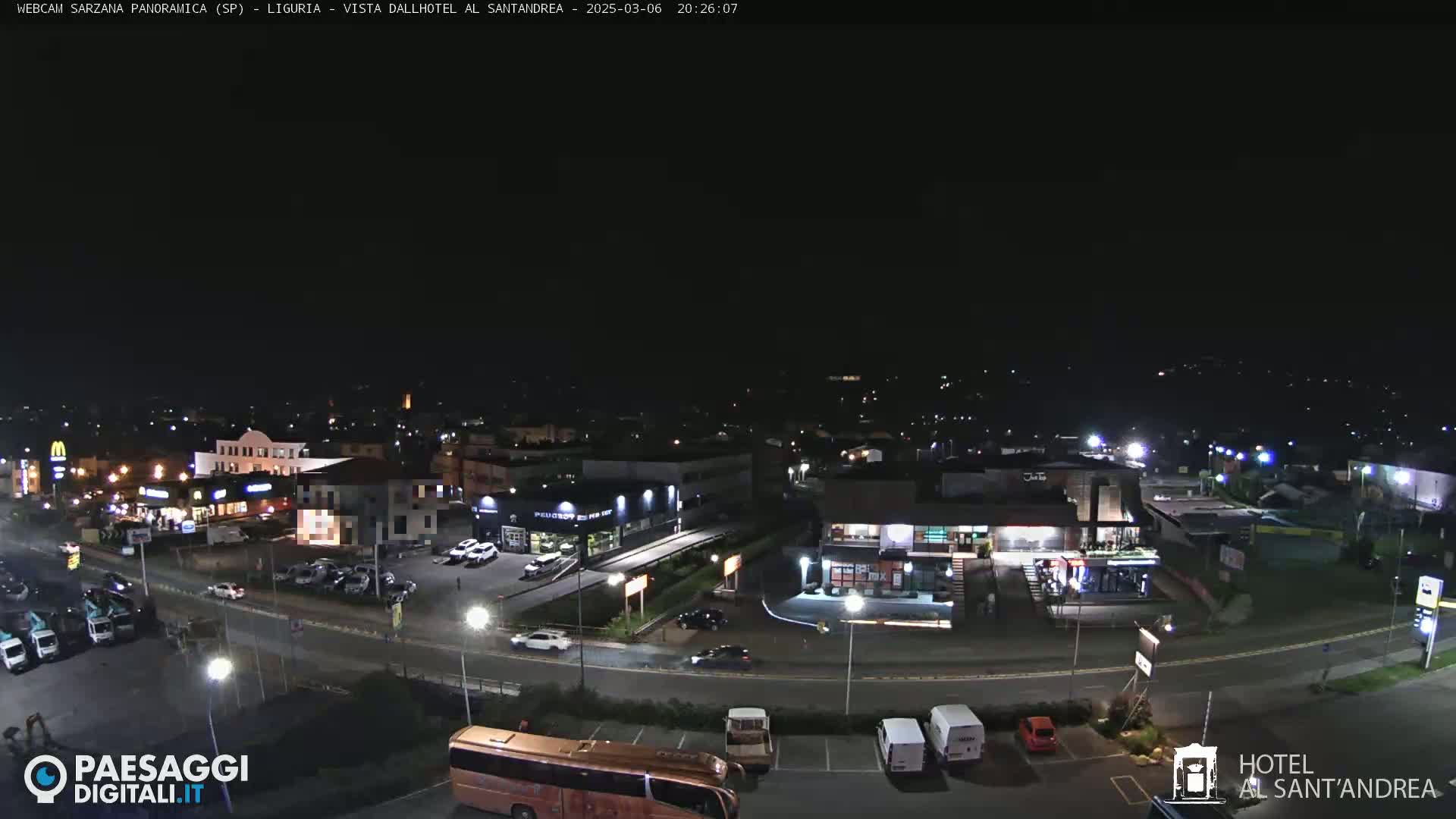 A nighttime aerial view of a town's illuminated streets and buildings, including a parking lot and a bus.
