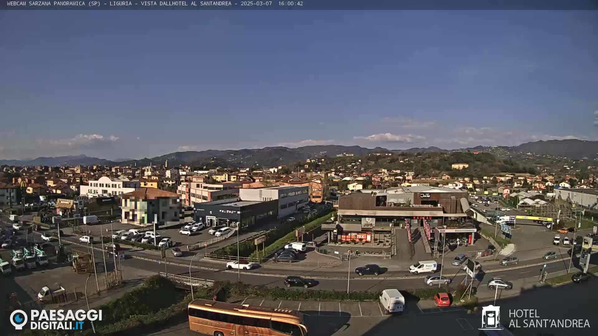 A sunny day reveals a panoramic view of a town nestled among hills, with roads, buildings, and parked cars visible.