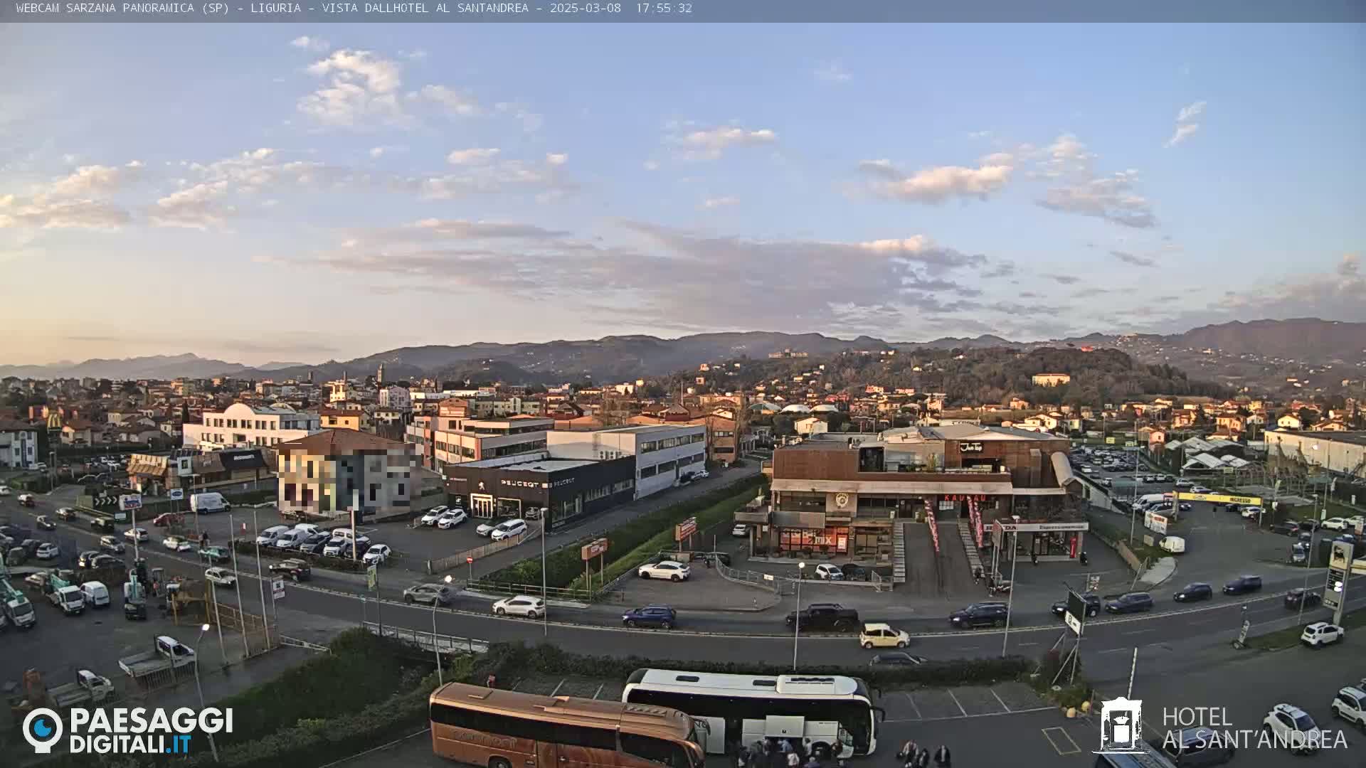 A partly cloudy sunset over a town with many buildings and cars, including a large bus in a parking lot.