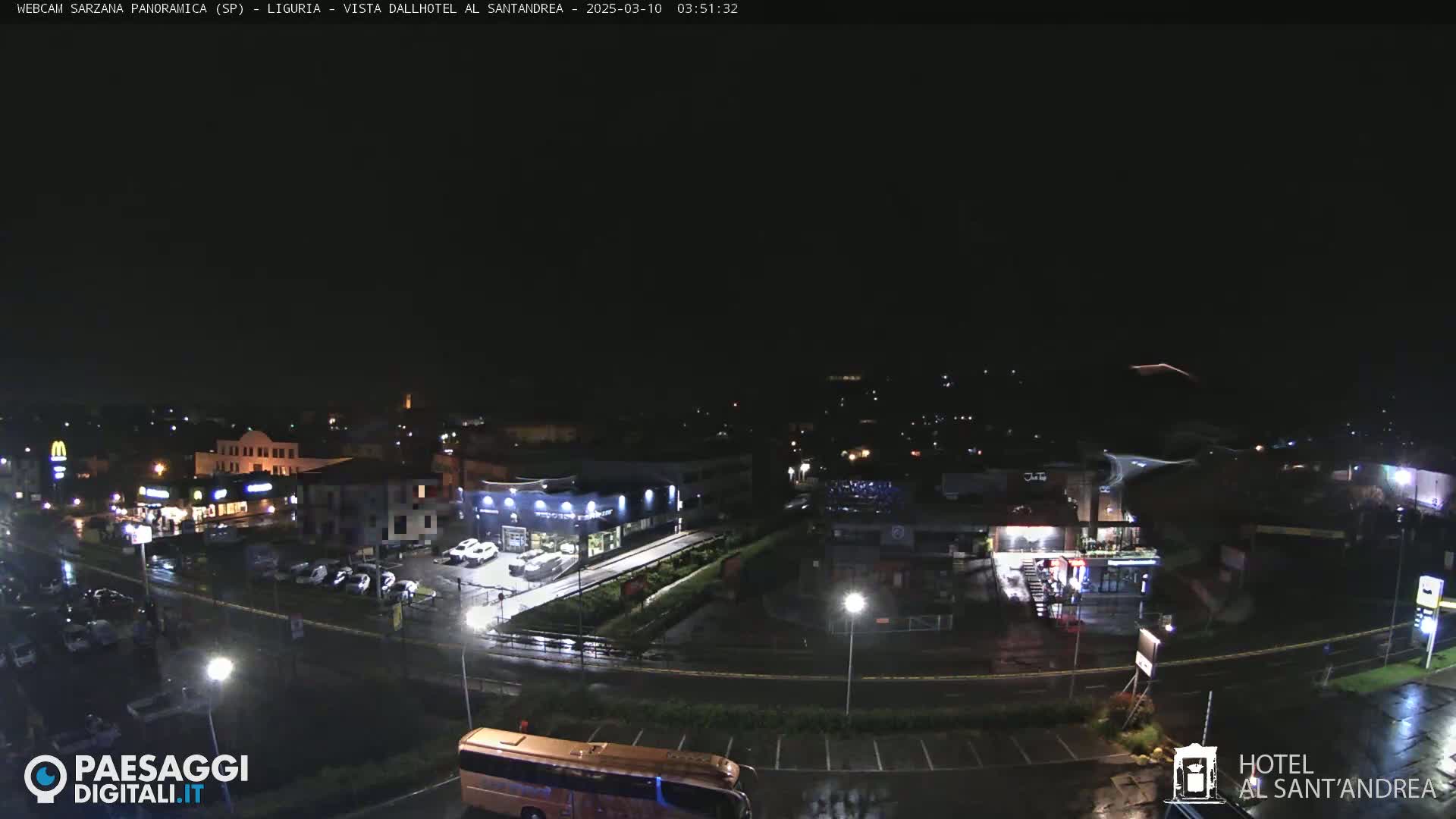A nighttime, wet view of a town with cars parked in lots and a bus visible in the lower right corner.