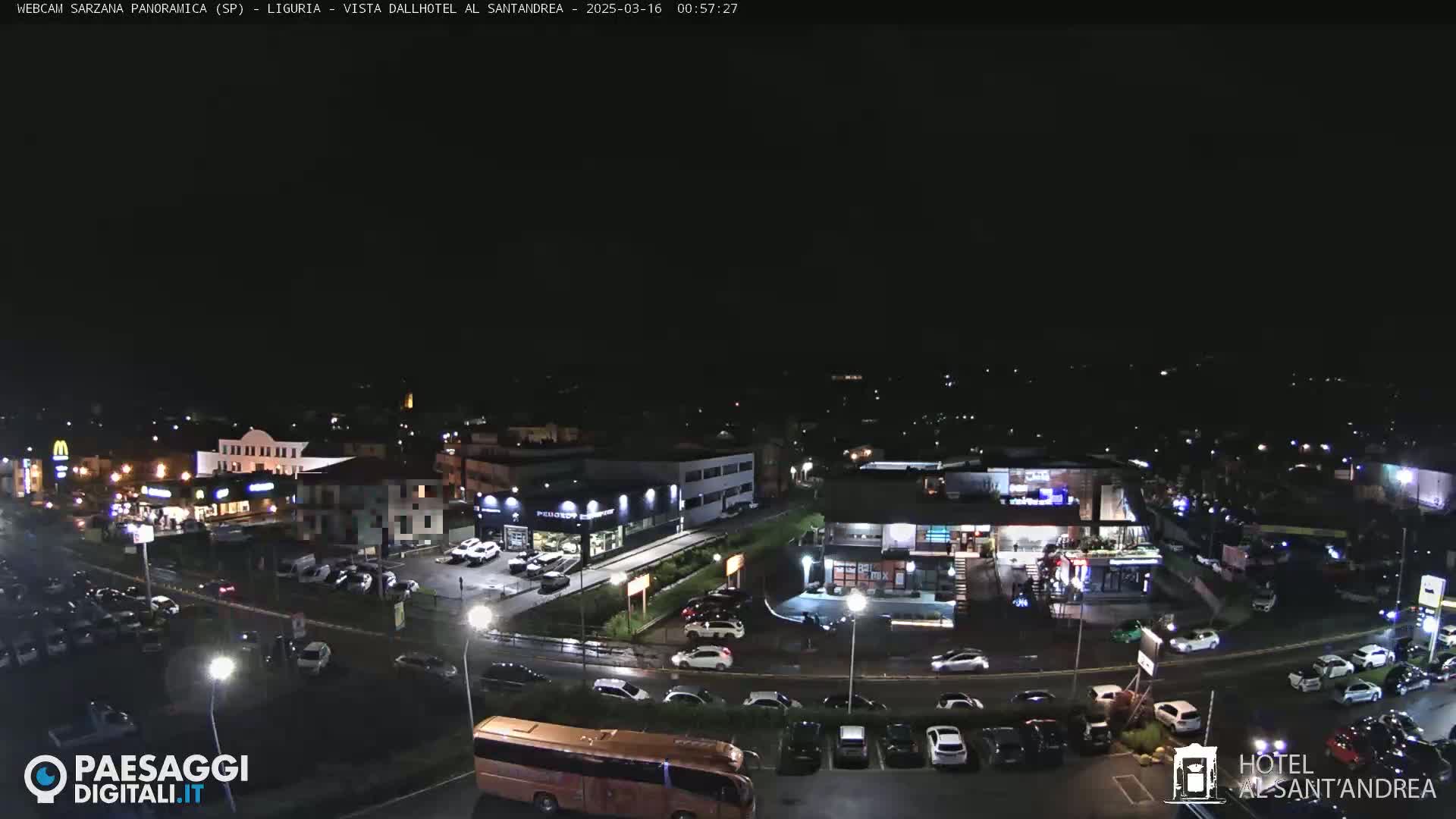 A nighttime aerial view of a town with several buildings, parking lots filled with cars, and a large bus, under a clear, dark sky.