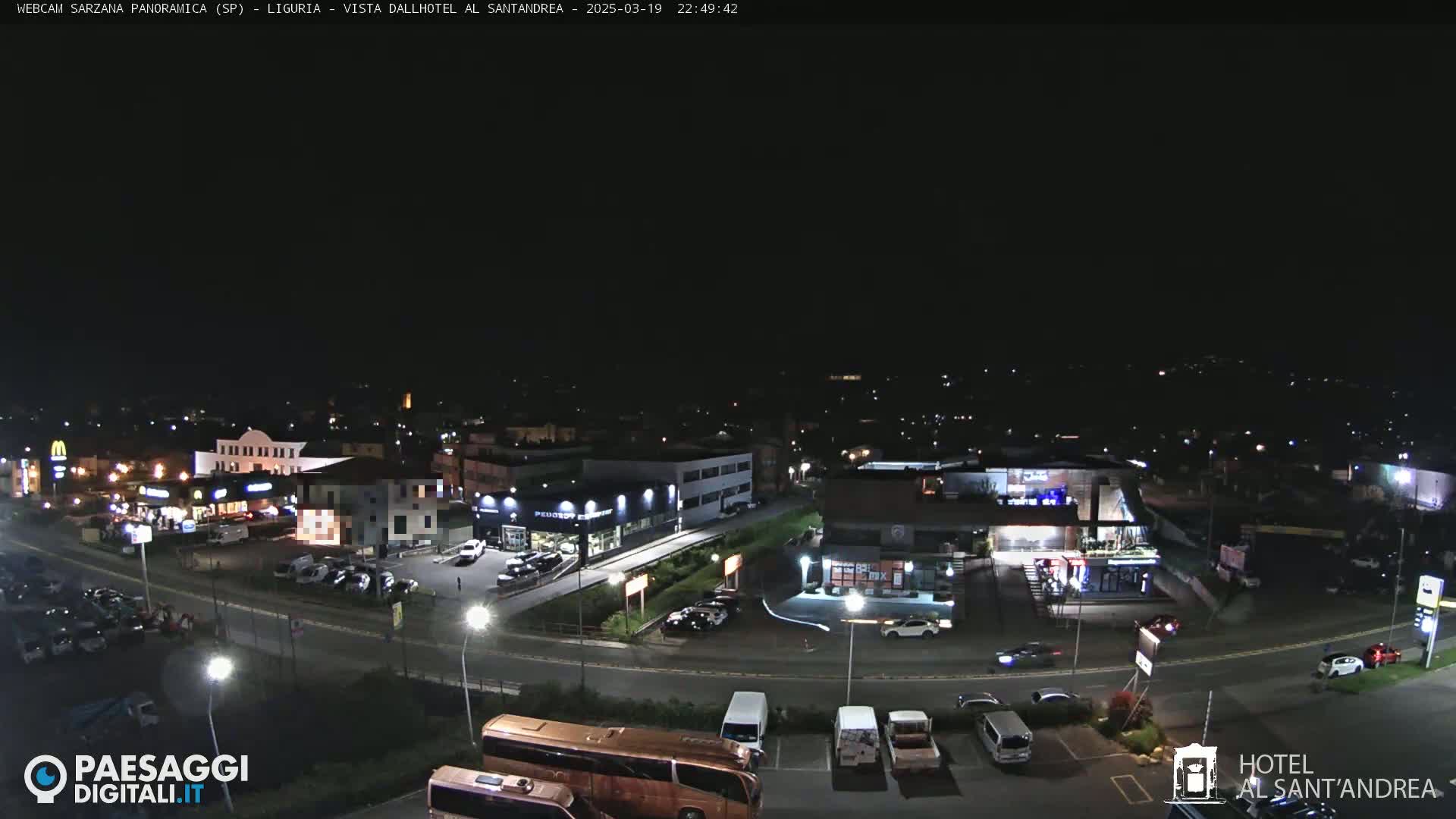 A nighttime, aerial view of a town's road and parking lots with several buildings and cars.