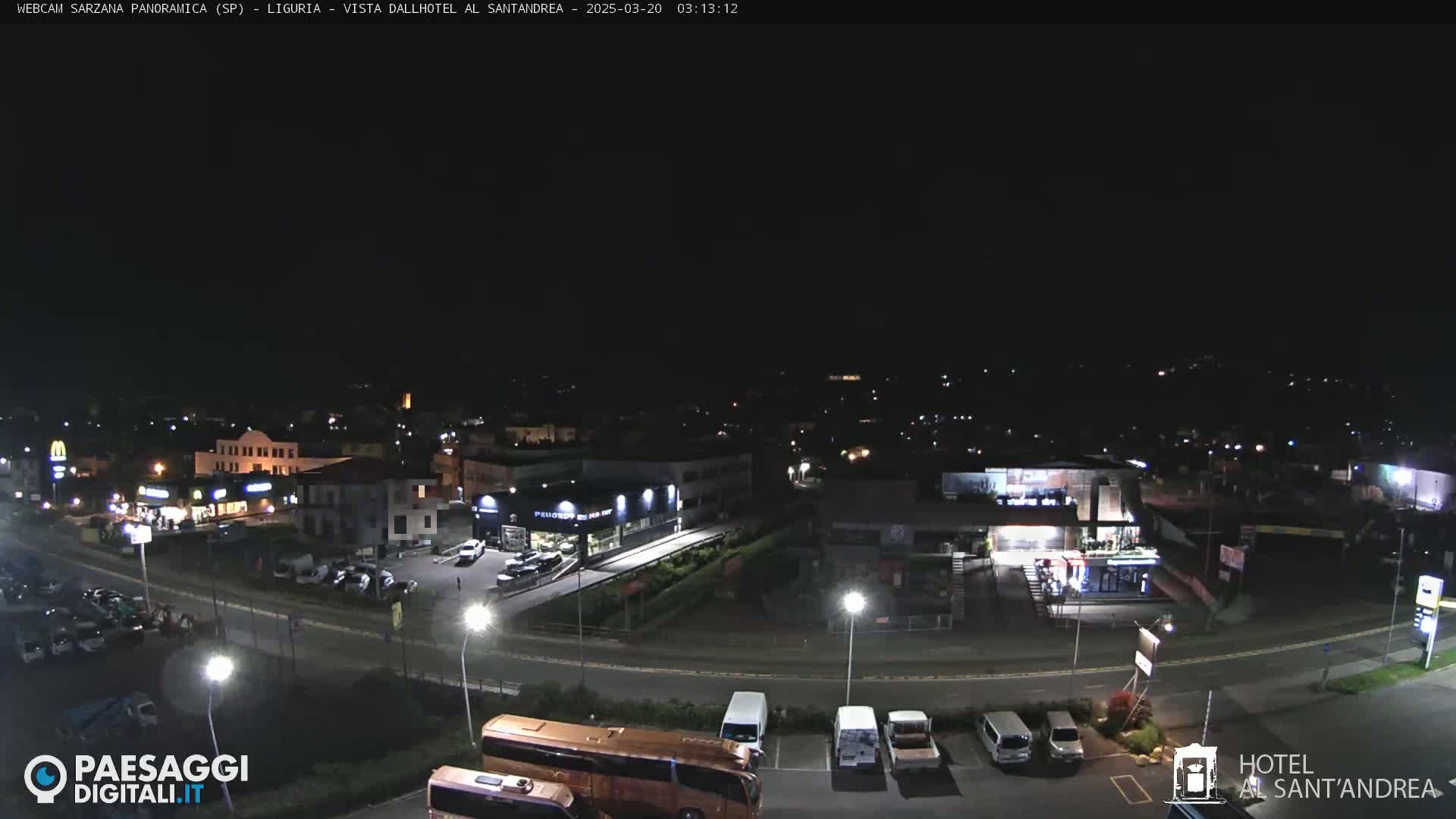 A nighttime aerial view of a town's street and parking lot, with various buildings and vehicles visible under a clear, dark sky.