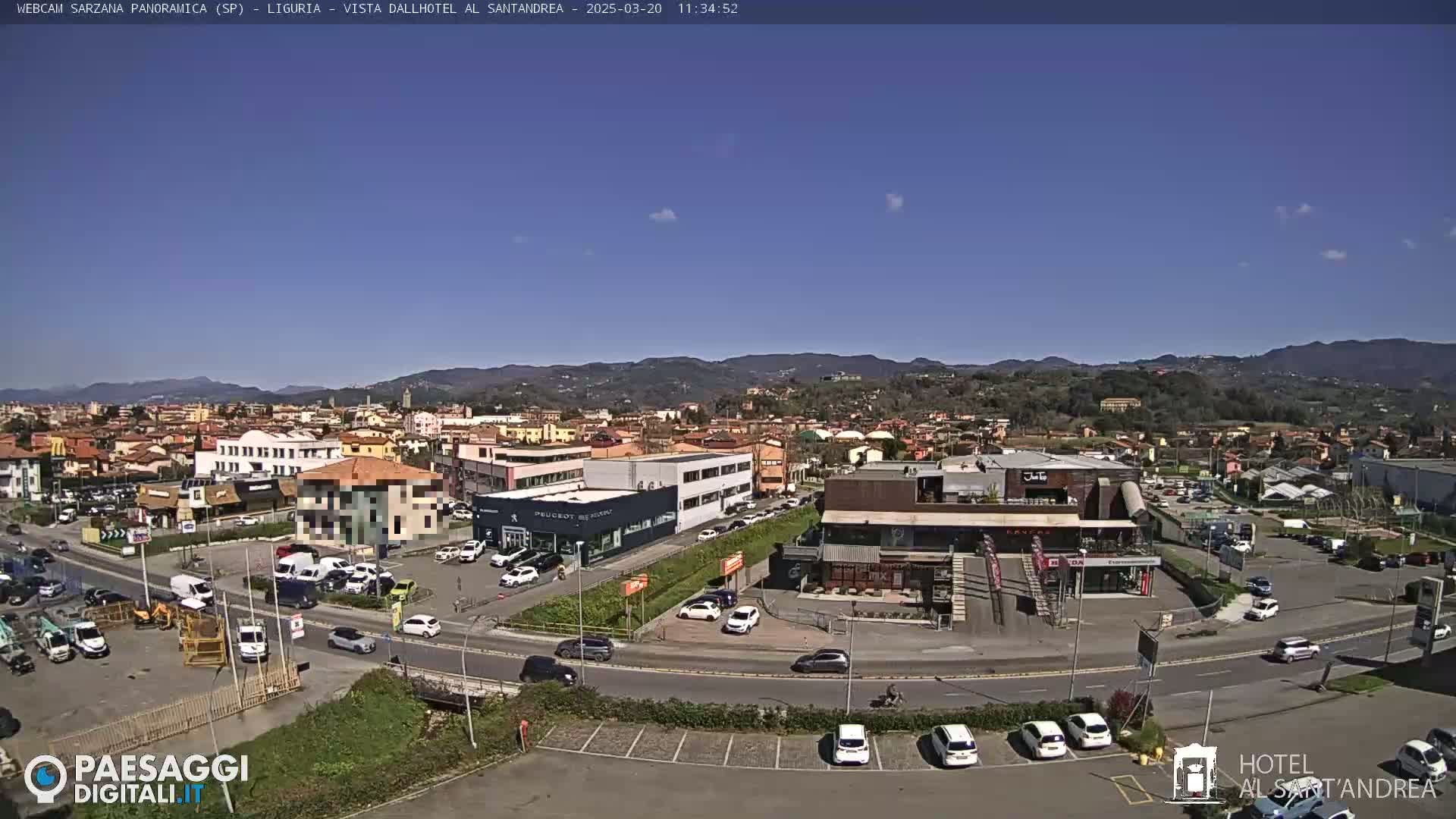 A sunny, clear day reveals a panoramic view of a town, with cars parked in lots surrounding various buildings and businesses near a roadway.