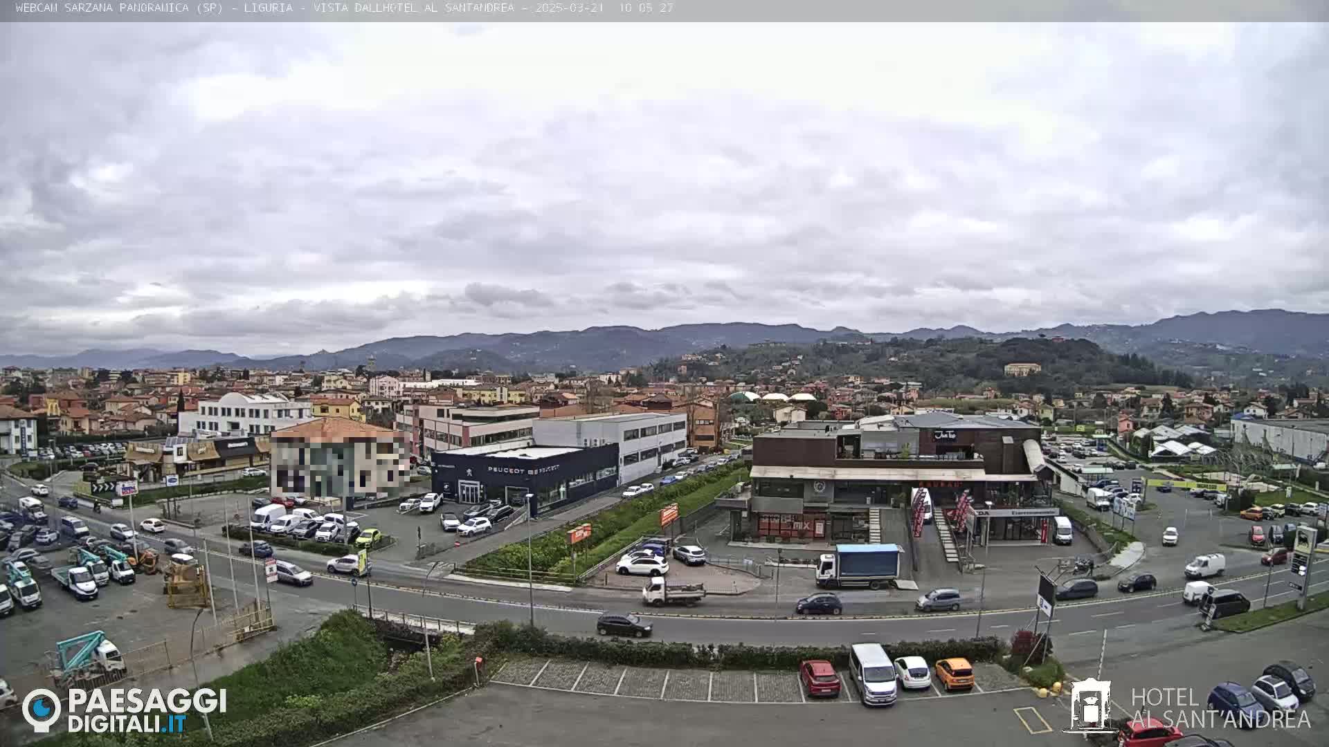 An overcast day reveals a town's cityscape, including buildings, roads, and parked cars, nestled at the base of distant hills.