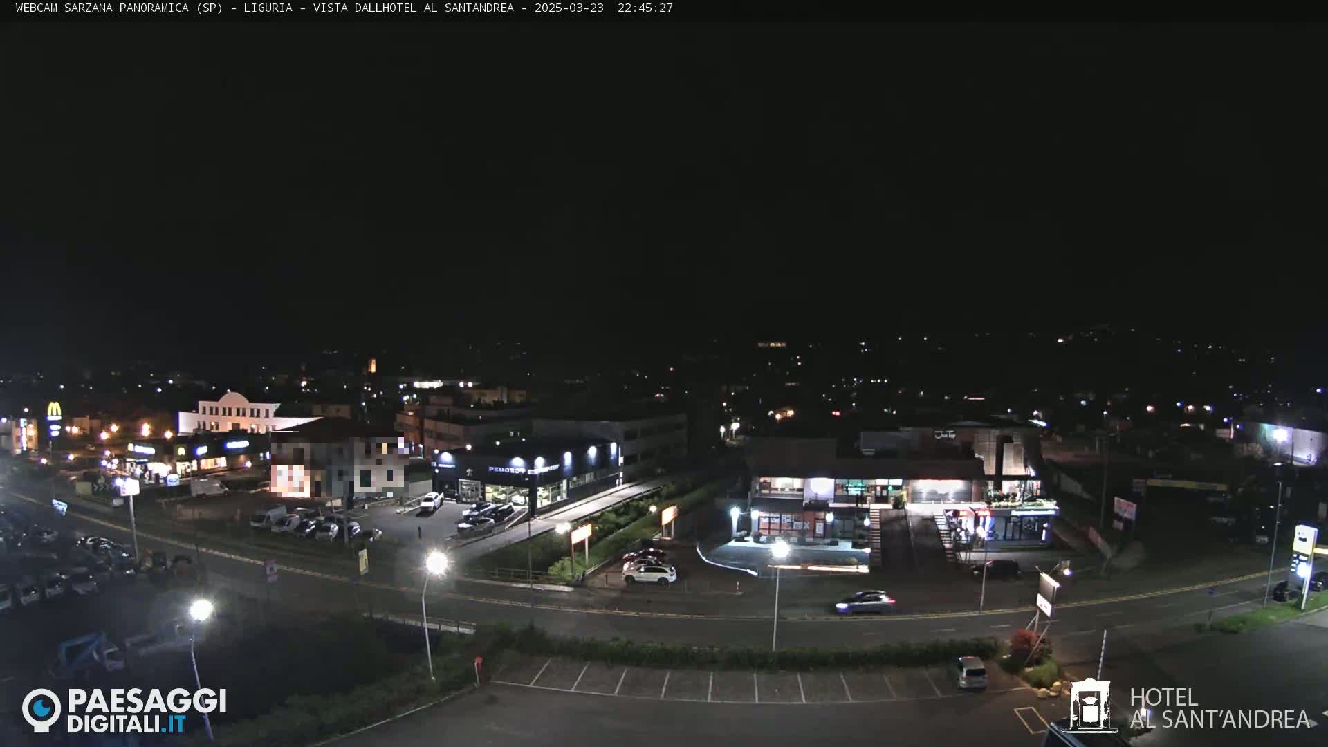 A nighttime aerial view of a town's street scene showing cars parked in lots near illuminated buildings and businesses.