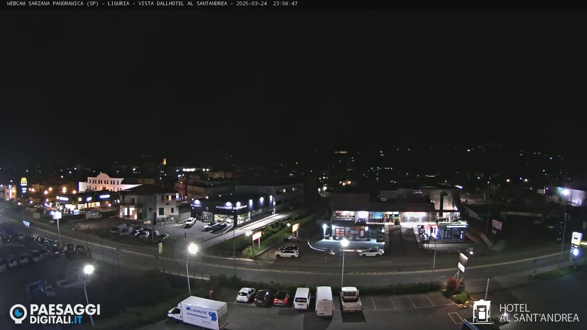 A nighttime, aerial view of a town with various businesses and parked cars along roads and parking lots.