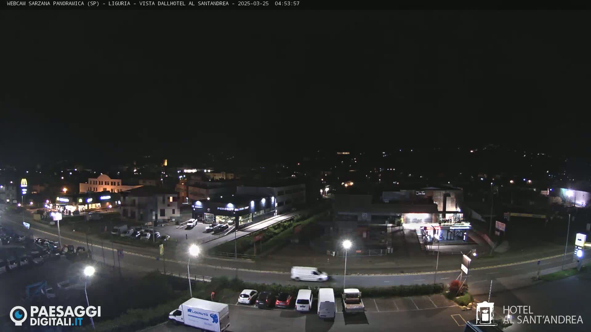 A nighttime aerial view of a town with cars parked in lots and driving on roads, under a clear, dark sky.