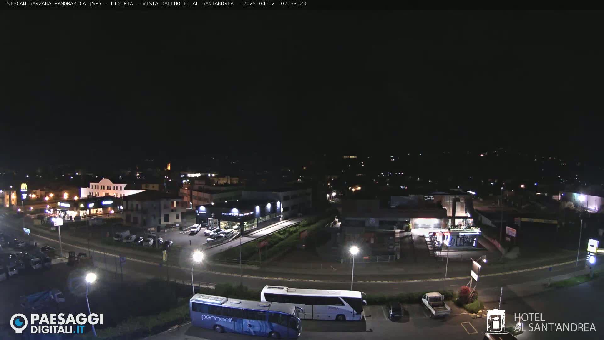 A nighttime aerial view of a town with streetlights illuminating roads, buildings, and parked cars and buses.