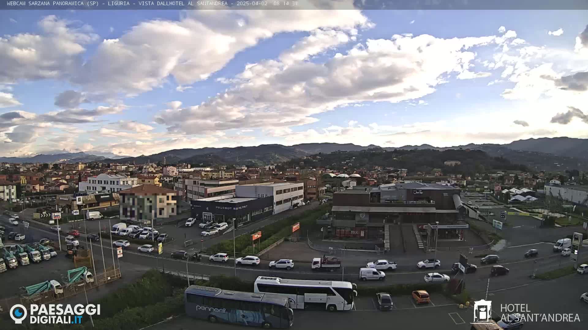 A partly cloudy sky overlooks a town with buildings, vehicles, and a large bus in a parking lot.
