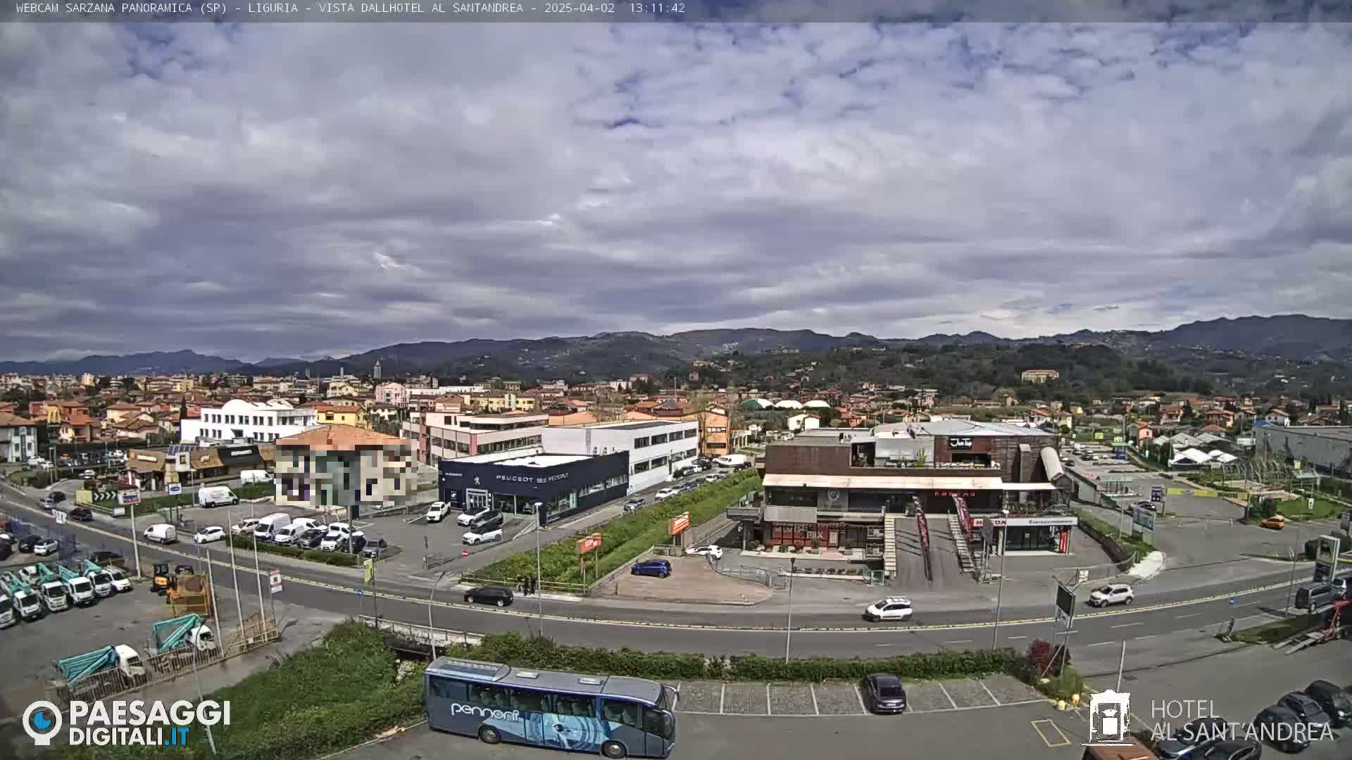 A partly cloudy day reveals a panoramic view of a town nestled among hills, featuring a mix of residential and commercial buildings, with vehicles in parking lots and on roads.