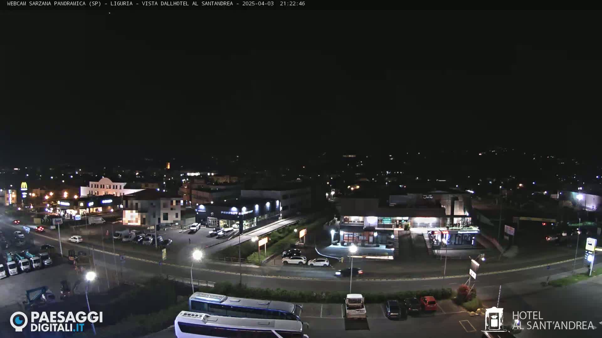 A nighttime, overhead view of a road intersection near several buildings and businesses, including a hotel and fast-food restaurants, under a clear, dark sky.