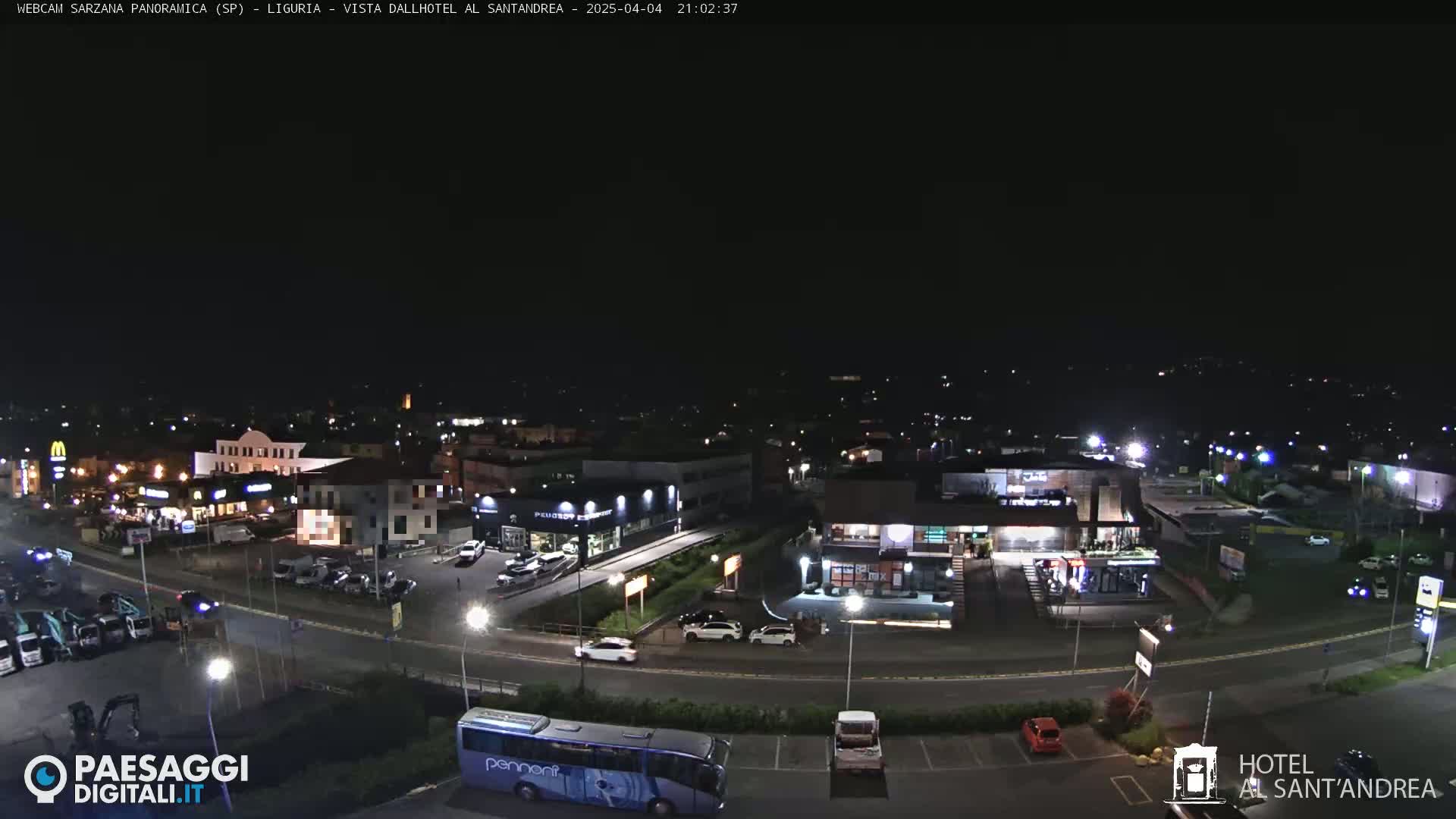A nighttime aerial view of a town's outskirts, showing illuminated buildings, parking lots, and roadways.