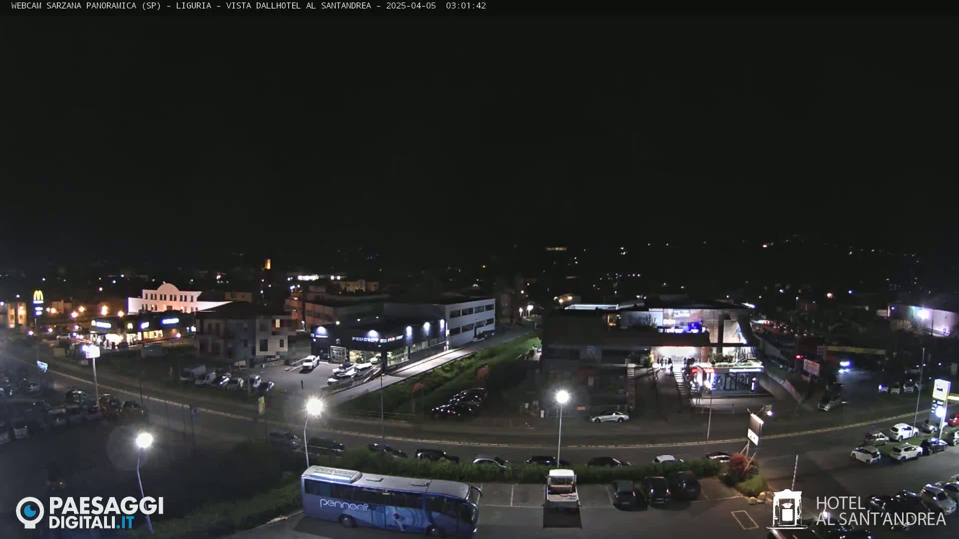 A nighttime aerial view of a town's outskirts, showing parking lots, buildings, and roads with cars, under a clear, dark sky.