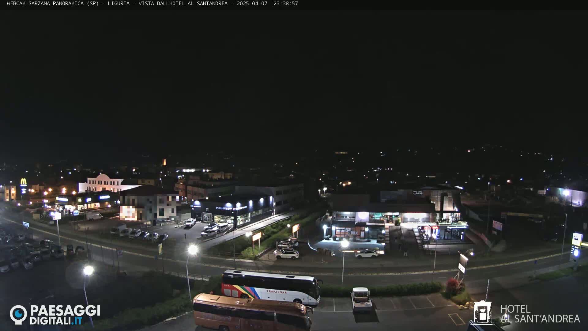 A nighttime, high-angle view of a town's parking lot and surrounding businesses, with a large bus and a few cars visible under a clear, dark sky.