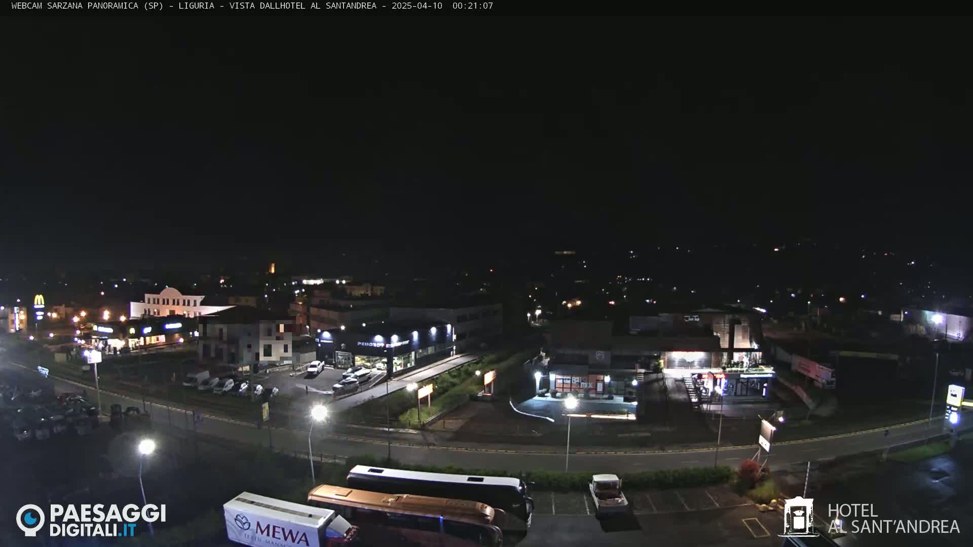 A nighttime, aerial view of a town with illuminated buildings, roads, and parked vehicles.