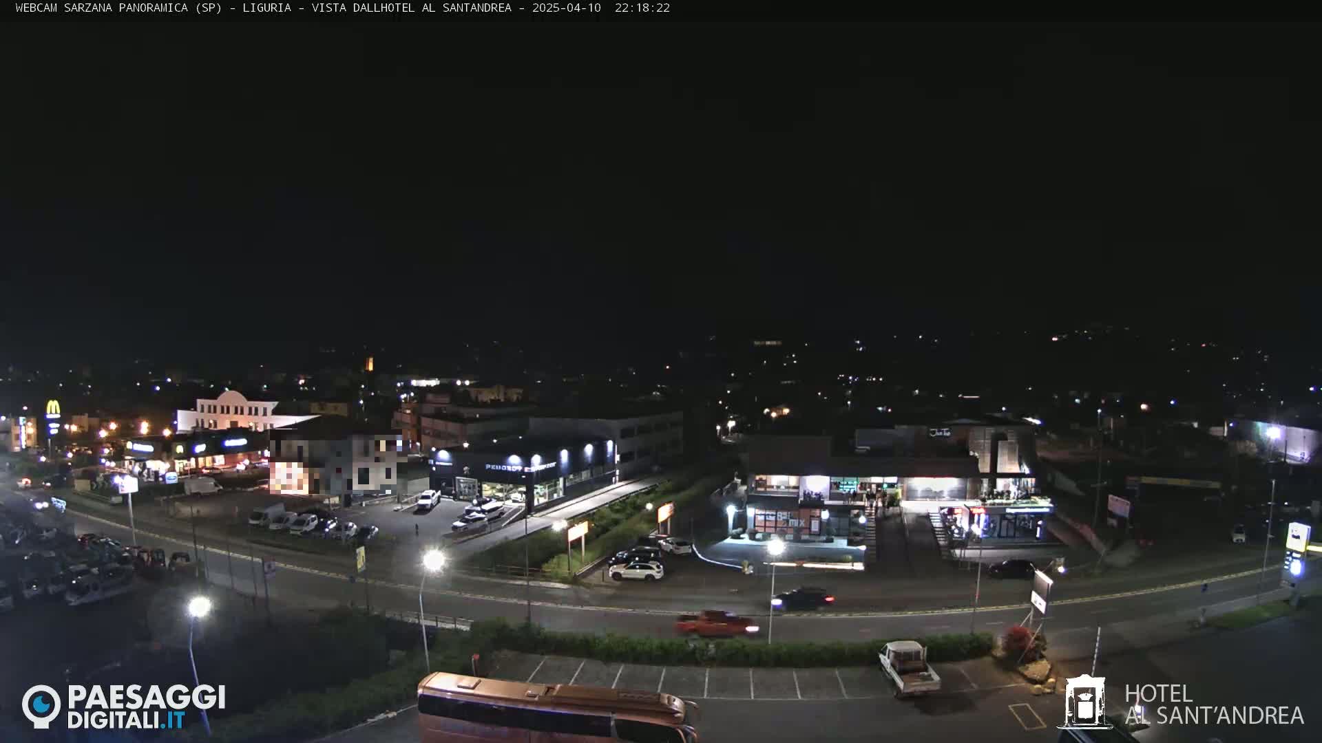 A nighttime, aerial view of a town's outskirts, showing roads, buildings, and parked cars under a clear, dark sky.