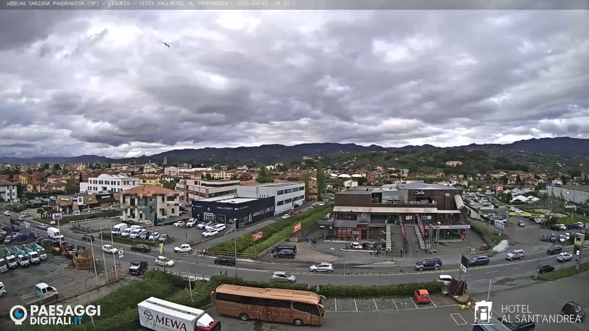 A wide shot of a town under a cloudy sky, showing buildings, vehicles, and a large bus in a parking lot.