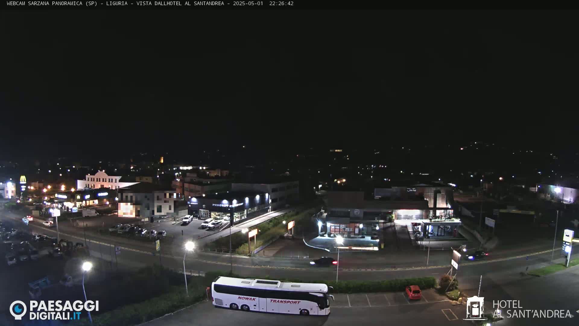 A nighttime, wide shot of a town's commercial area, including a bus and several buildings, under a dark sky.