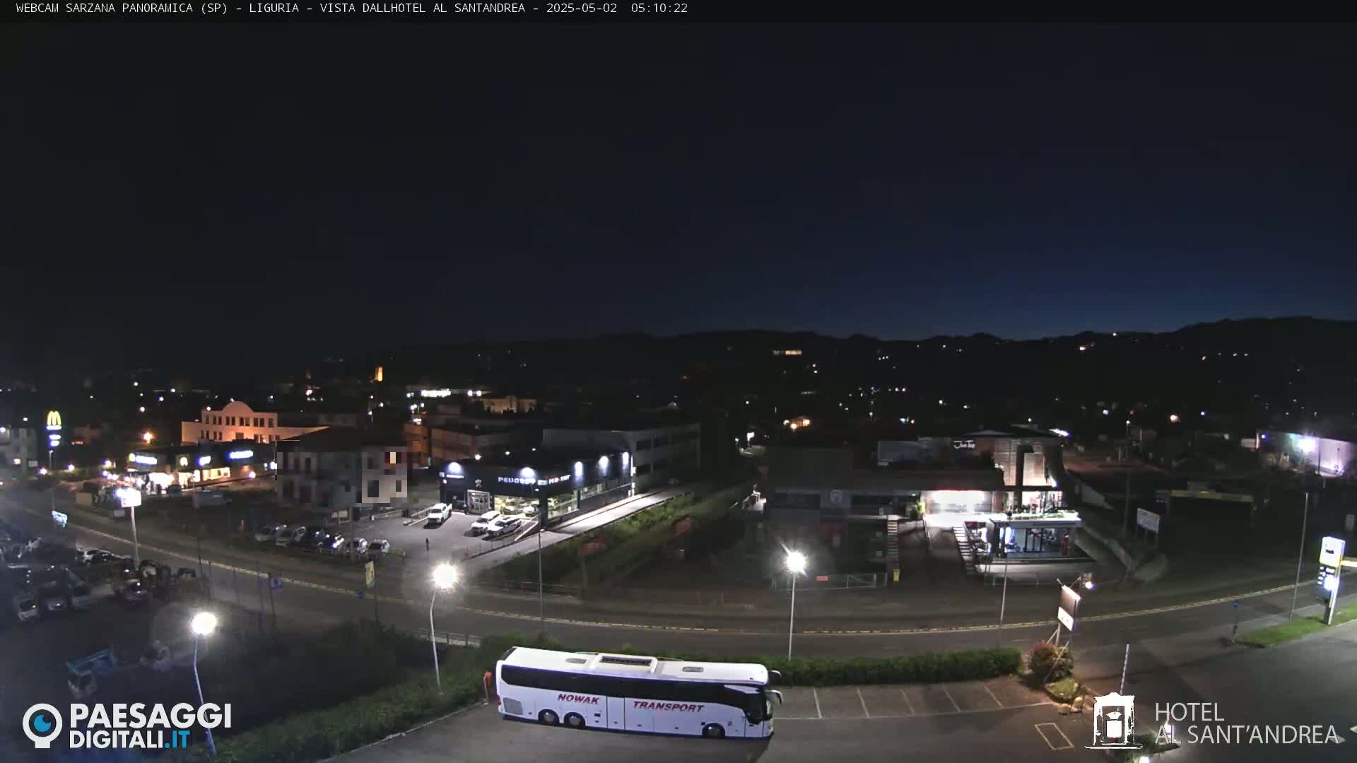 A nighttime, high-angle view of a town with buildings, parking lots, and a large bus parked near a hotel, under a dark, clear sky.