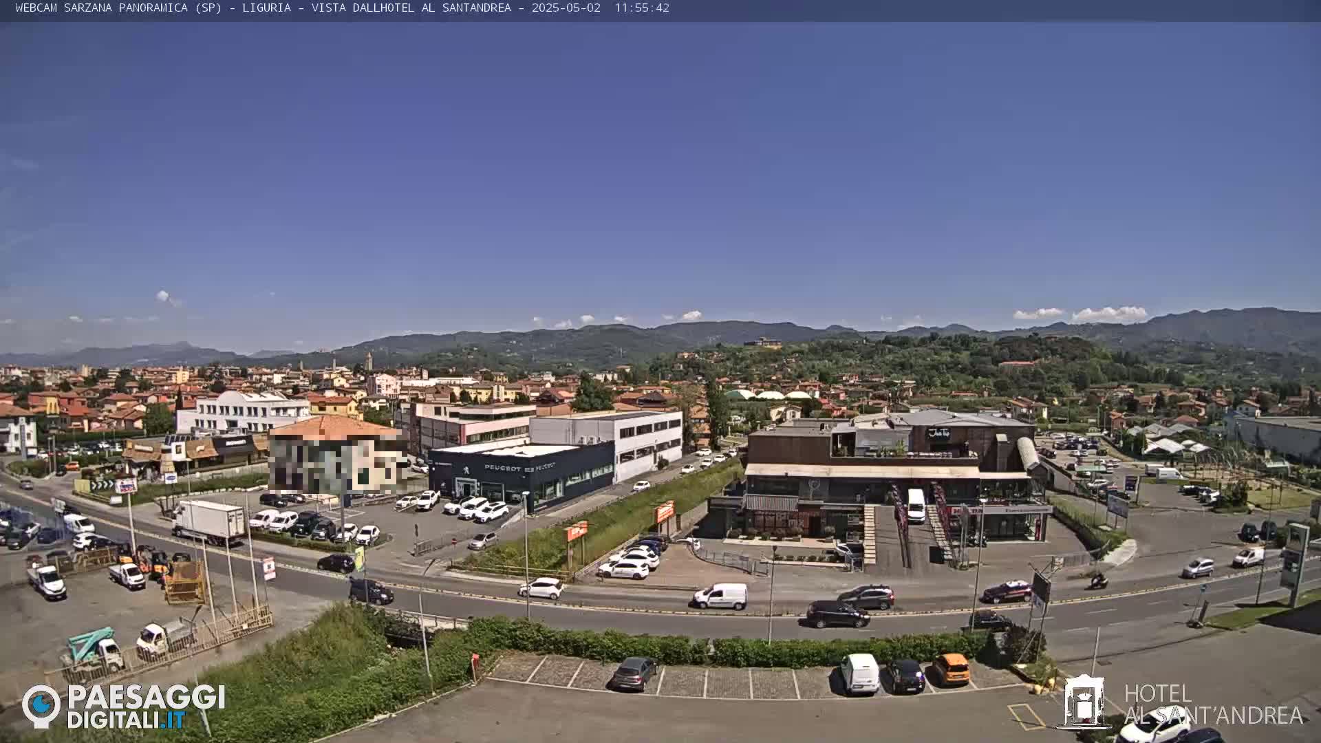 A sunny day reveals a panoramic view of a town nestled in a valley, with mountains in the background and cars parked in lots surrounding various buildings.