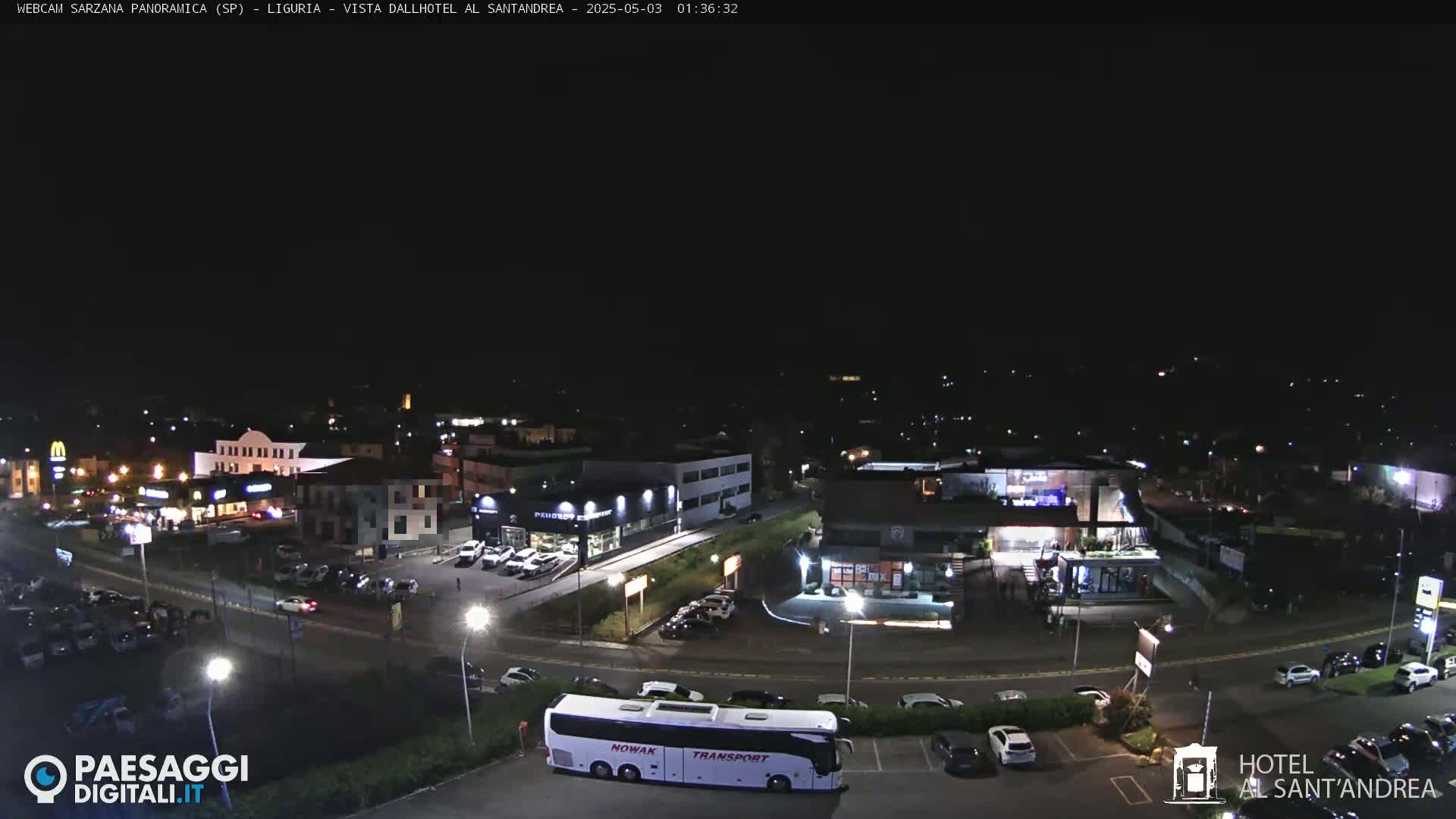 A nighttime aerial view of a town with buildings, roads, parked cars, and a bus.