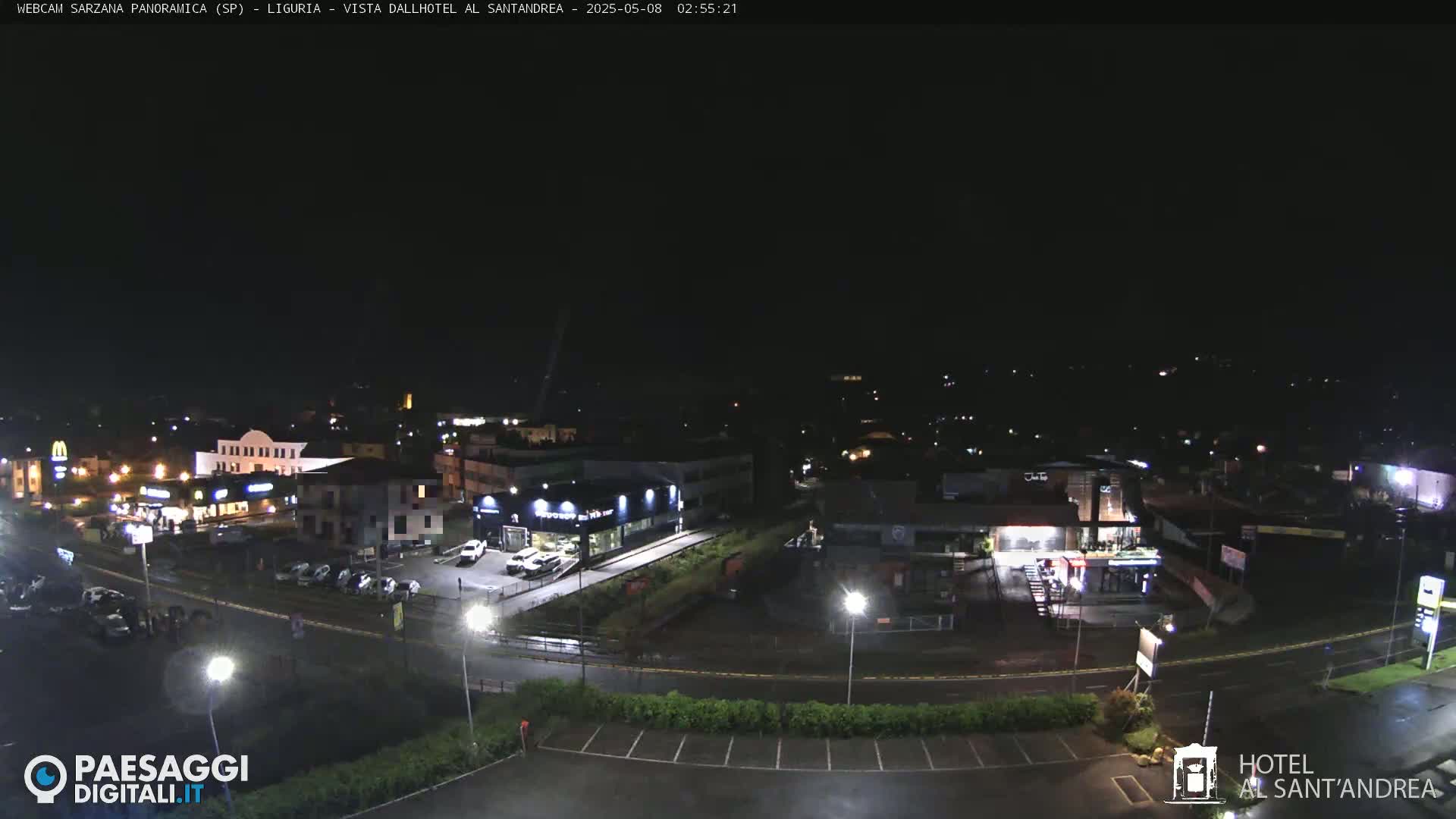 A nighttime, overhead view of a town with illuminated buildings and streets, and a parking lot.